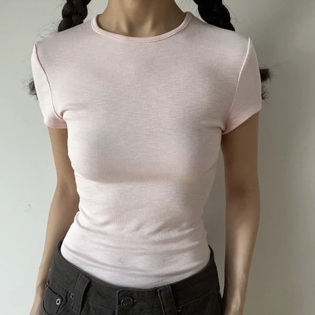 Lifestyle shot of form-fitting light pink ribbed crew-neck short-sleeve t-shirt, tucked into jeans