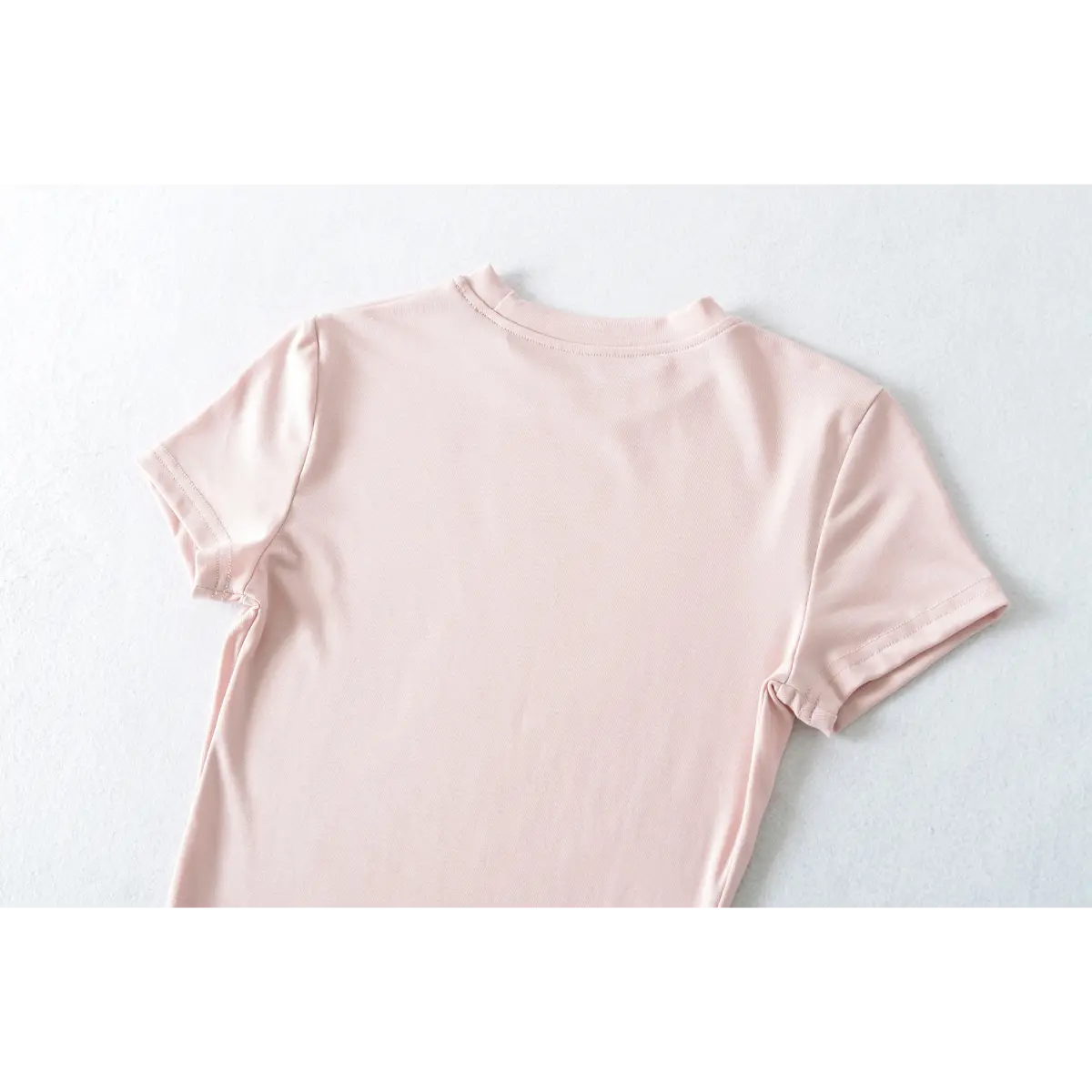 Partial back view of light pink ribbed t-shirt, showing neckline and shoulder seams