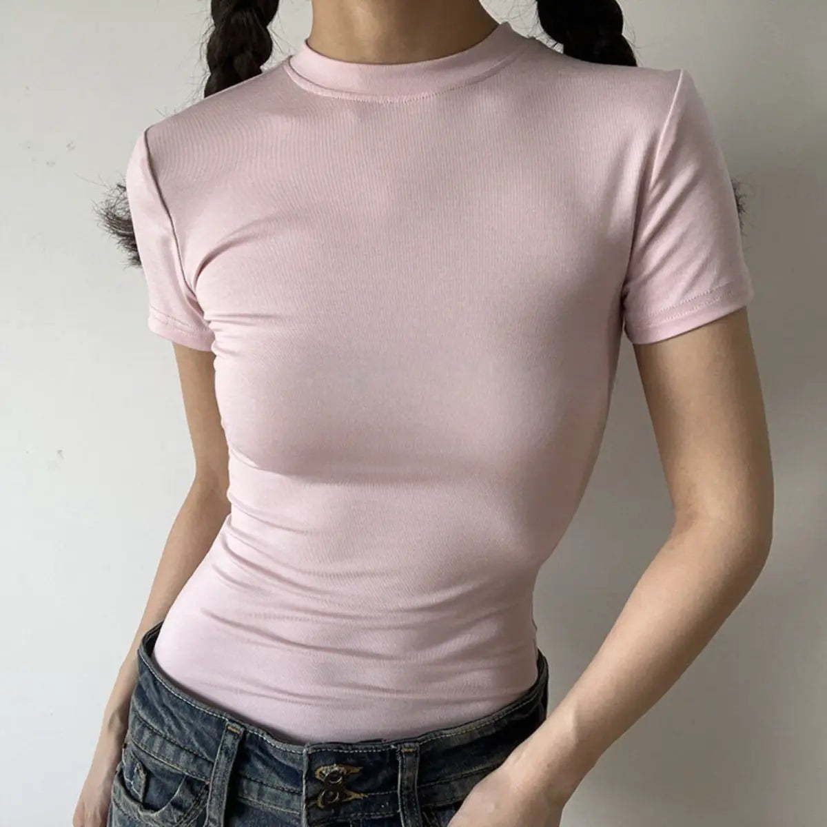 Lifestyle shot of form-fitting light pink ribbed crew-neck t-shirt, tucked into jeans