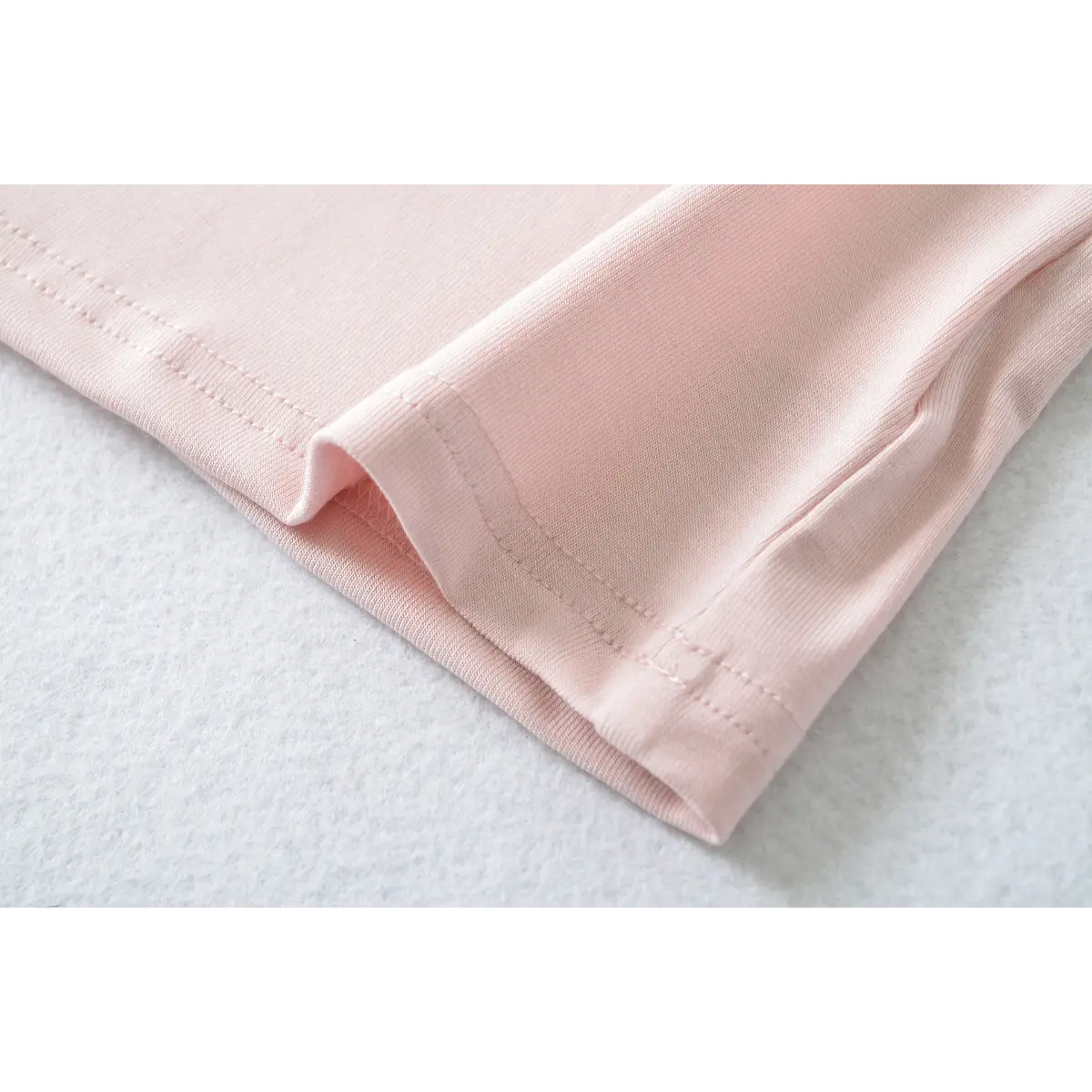 Close-up of light pink ribbed t-shirt's hem, showing fabric texture and stitching