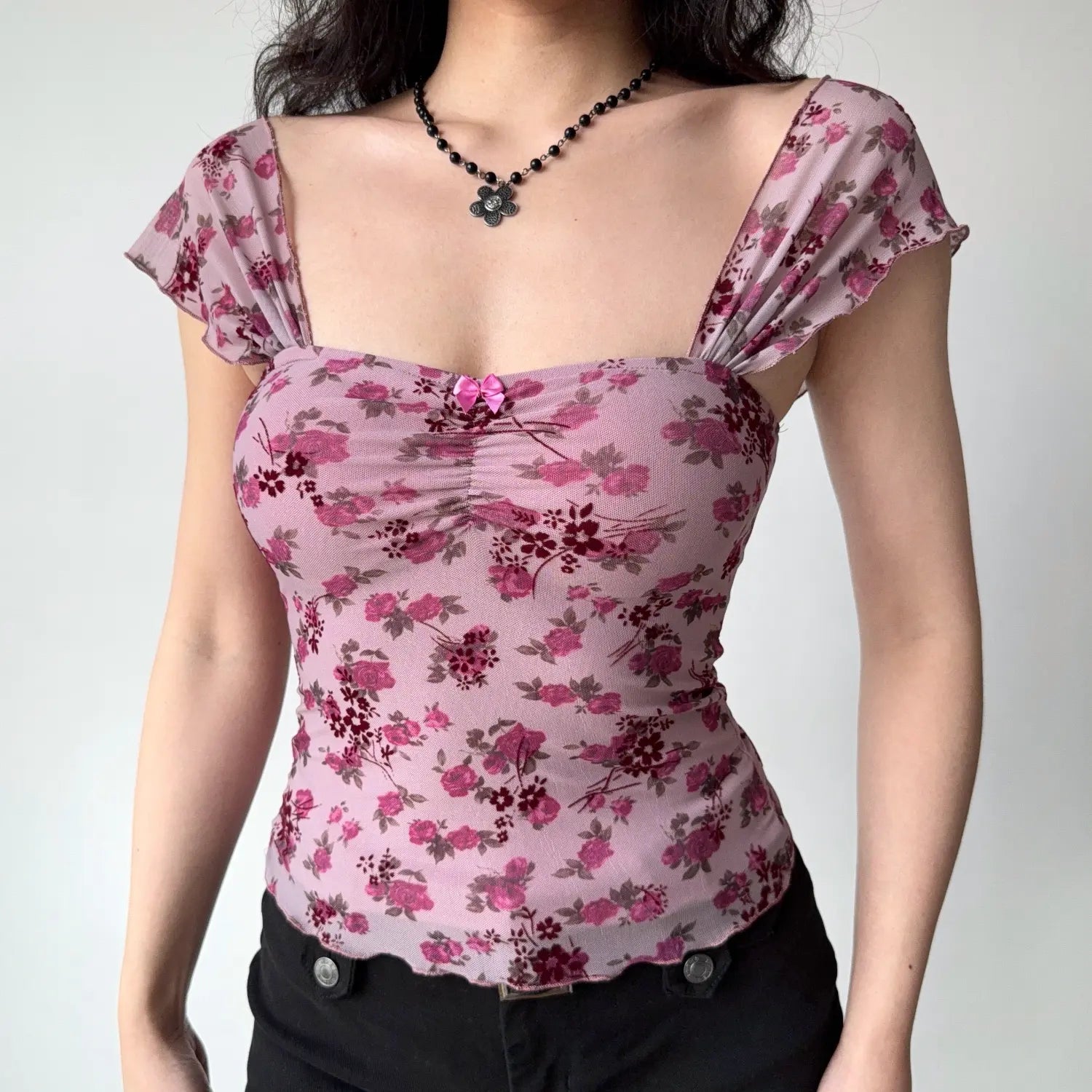 Front lifestyle shot on model of light pink rose floral mesh top, flutter cap sleeves, front mini bow decor, curved wavy hem