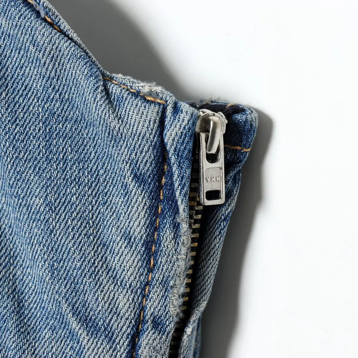 Close-up of the side YKK zipper on the light wash denim spaghetti strap dress, showing the metal pull and stitching