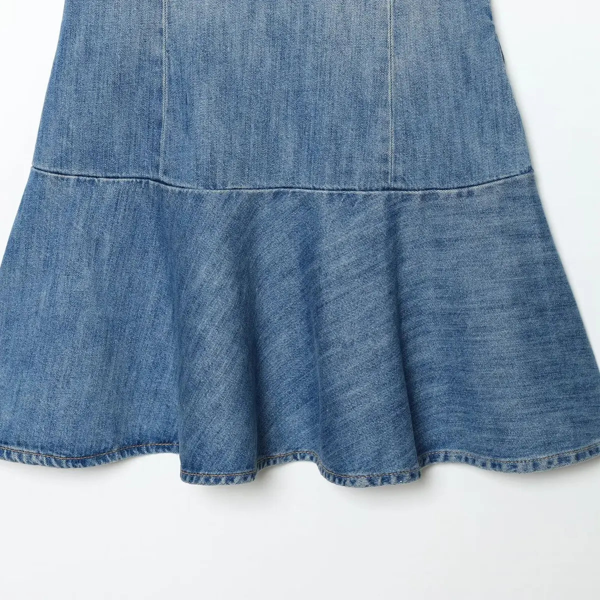 Skirt hem detail of light wash denim spaghetti strap dress, showing the flared ruffled hem and contrast stitching