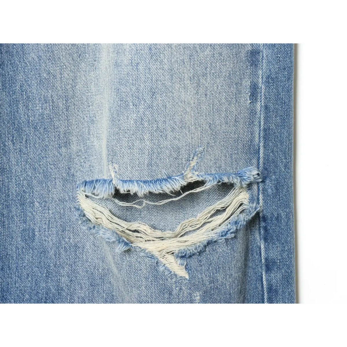 Close-up of frayed ripped knee hole with exposed white threads