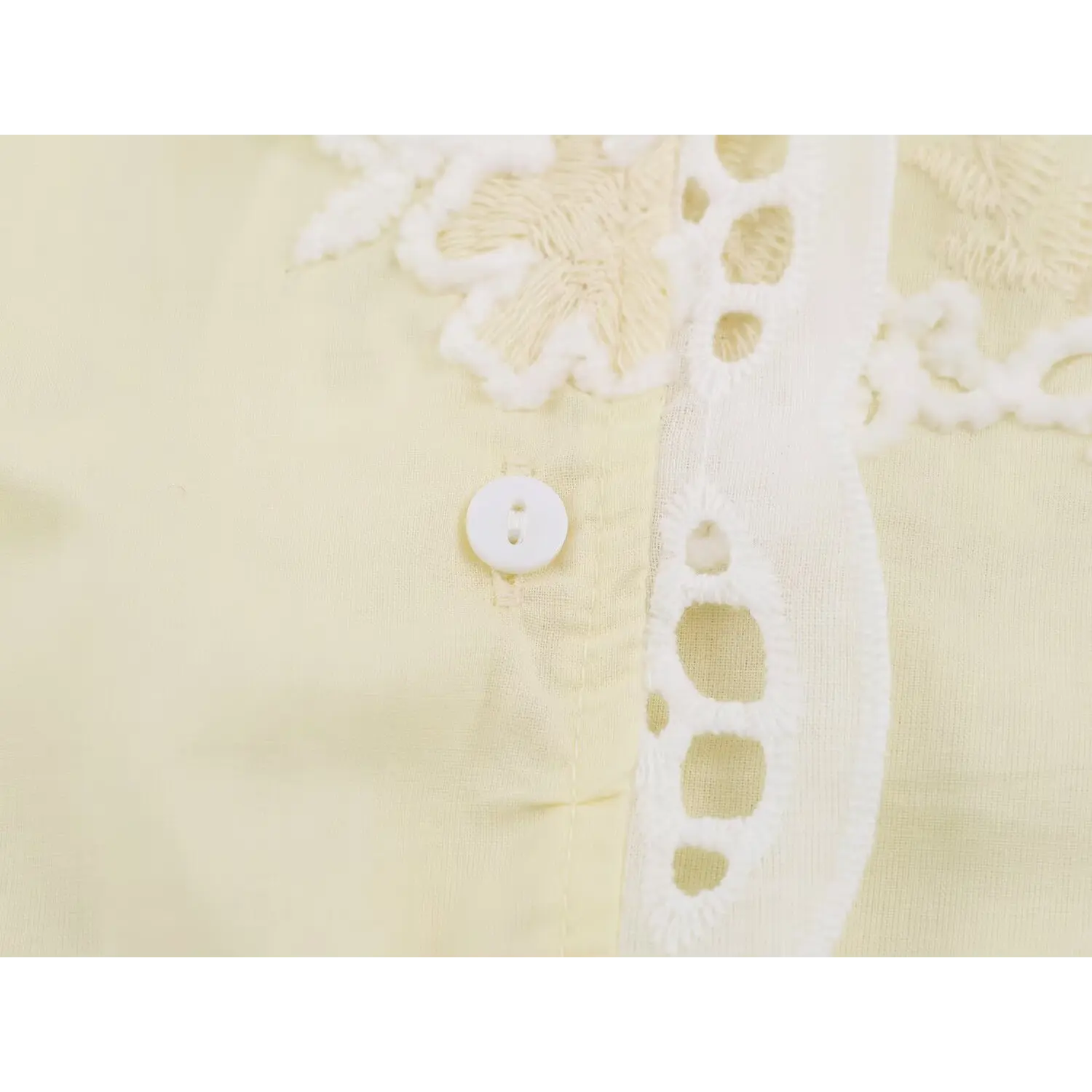 Closeup small white round front button, matching light yellow embroidered waistcoat textile