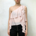 Model wears light pink one‑shoulder top with layered cascading ruffles