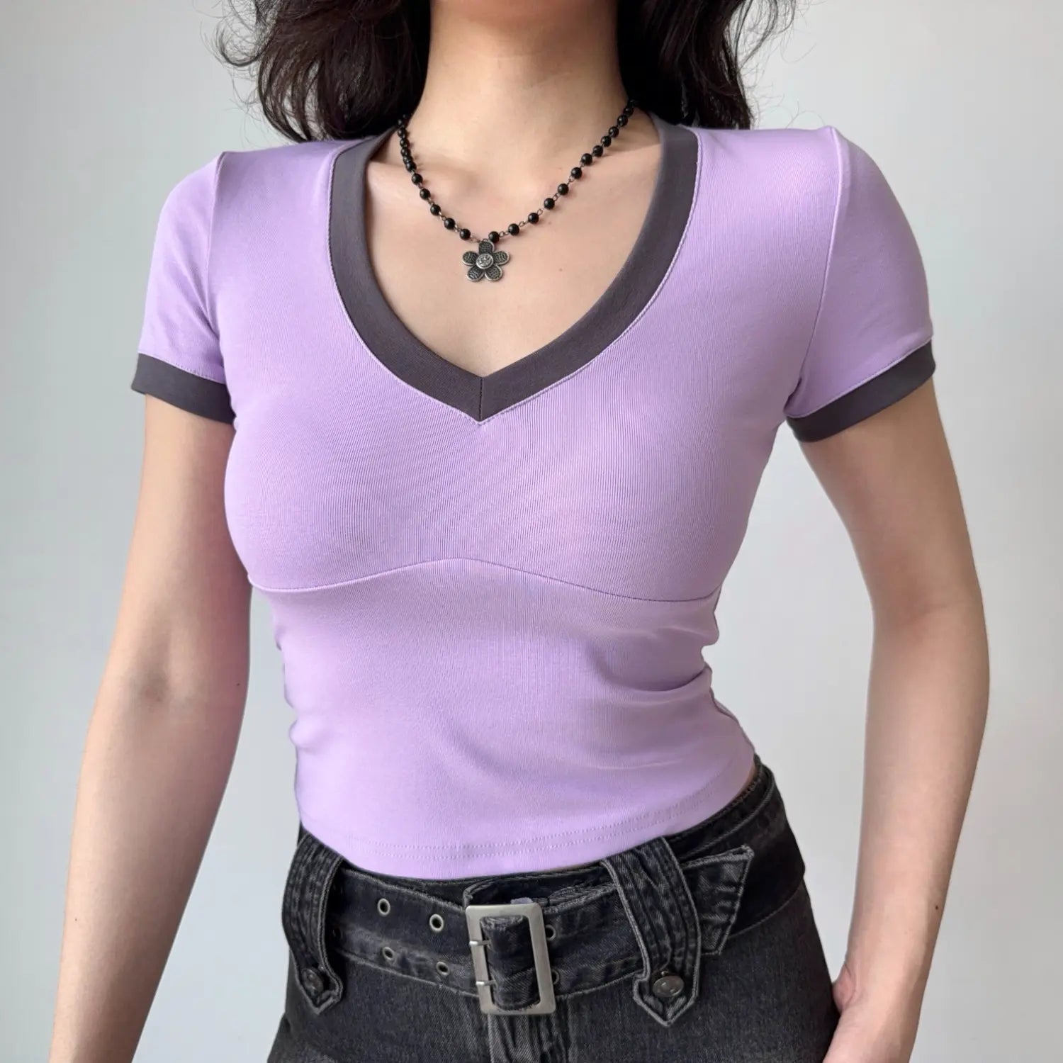 Full-body shot of a woman in a lilac fitted V-neck tee with dark gray trim, standing with hands relaxed at her sides