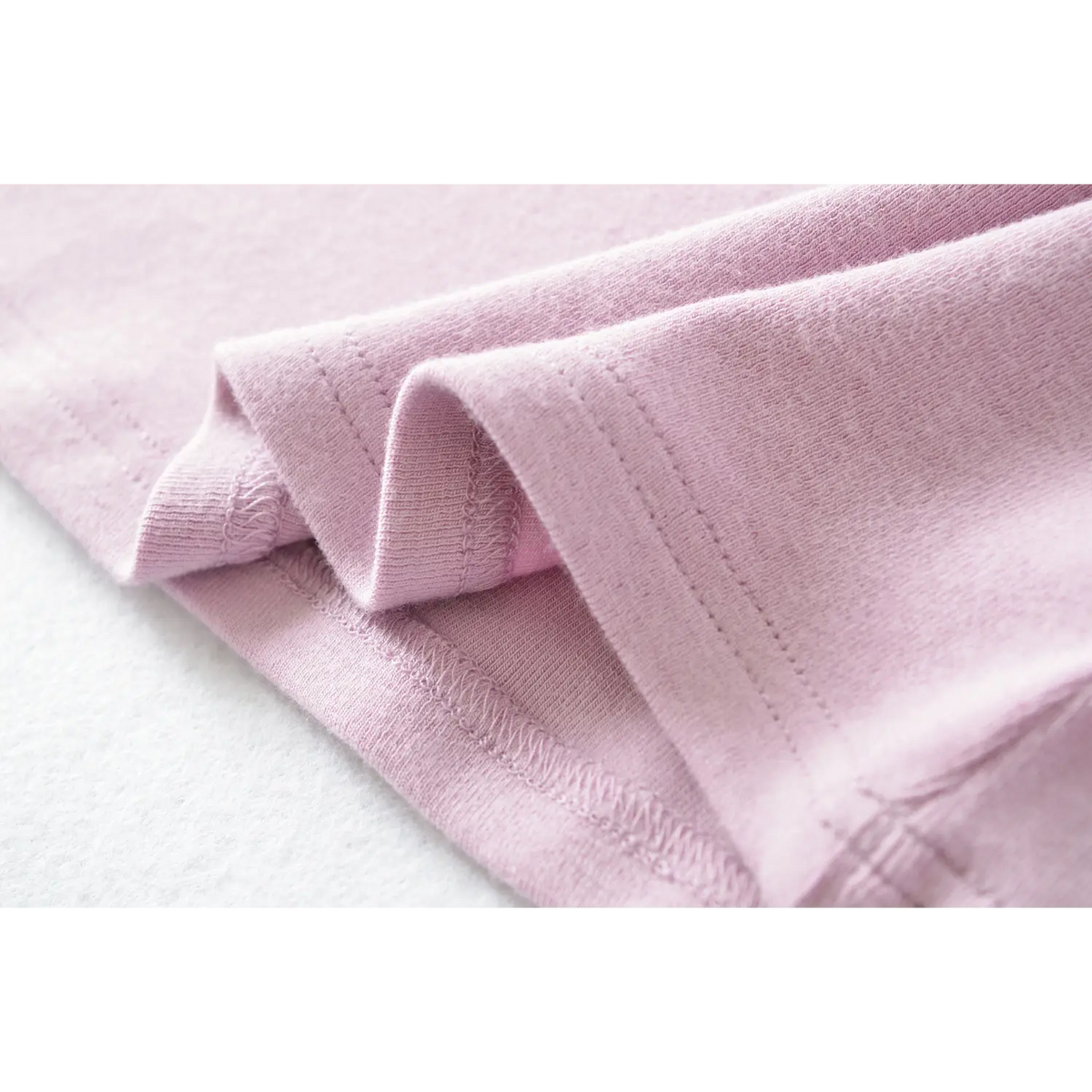 Detail shot of lilac women top bottom hem, folded fabric and fine serge stitching on soft knit material
