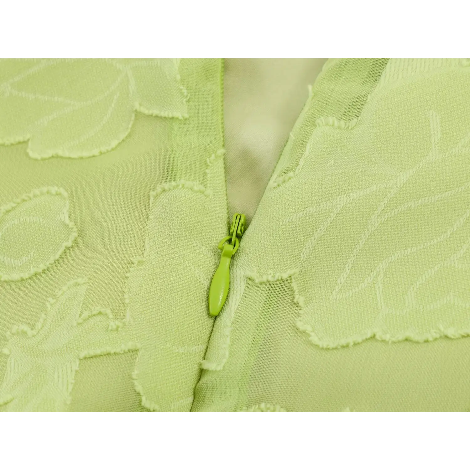 Macro shot of matching green invisible back zipper with elongated fabric pull tab, overlayed with raised floral sheer fabric