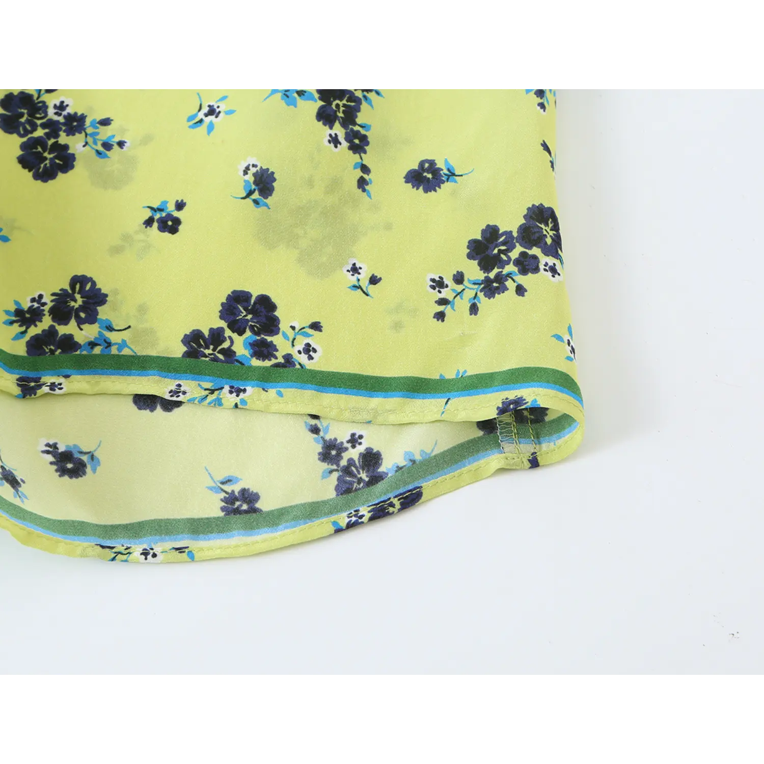 Extreme close‑up bottom hem contrast trim and stitching detail for lime green floral blouse