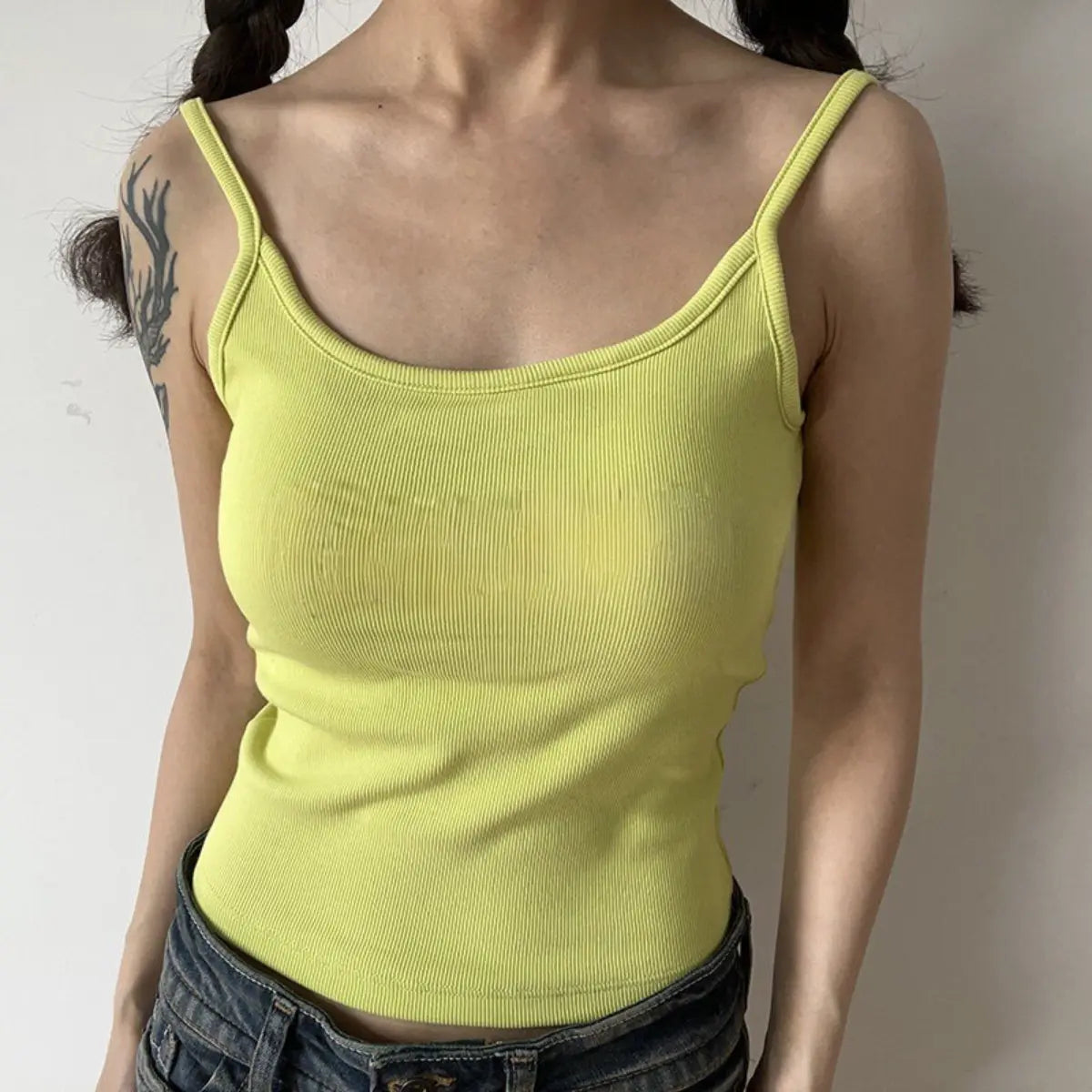 Lifestyle shot of form-fitting lime green ribbed camisole with thin straps, tucked into jeans