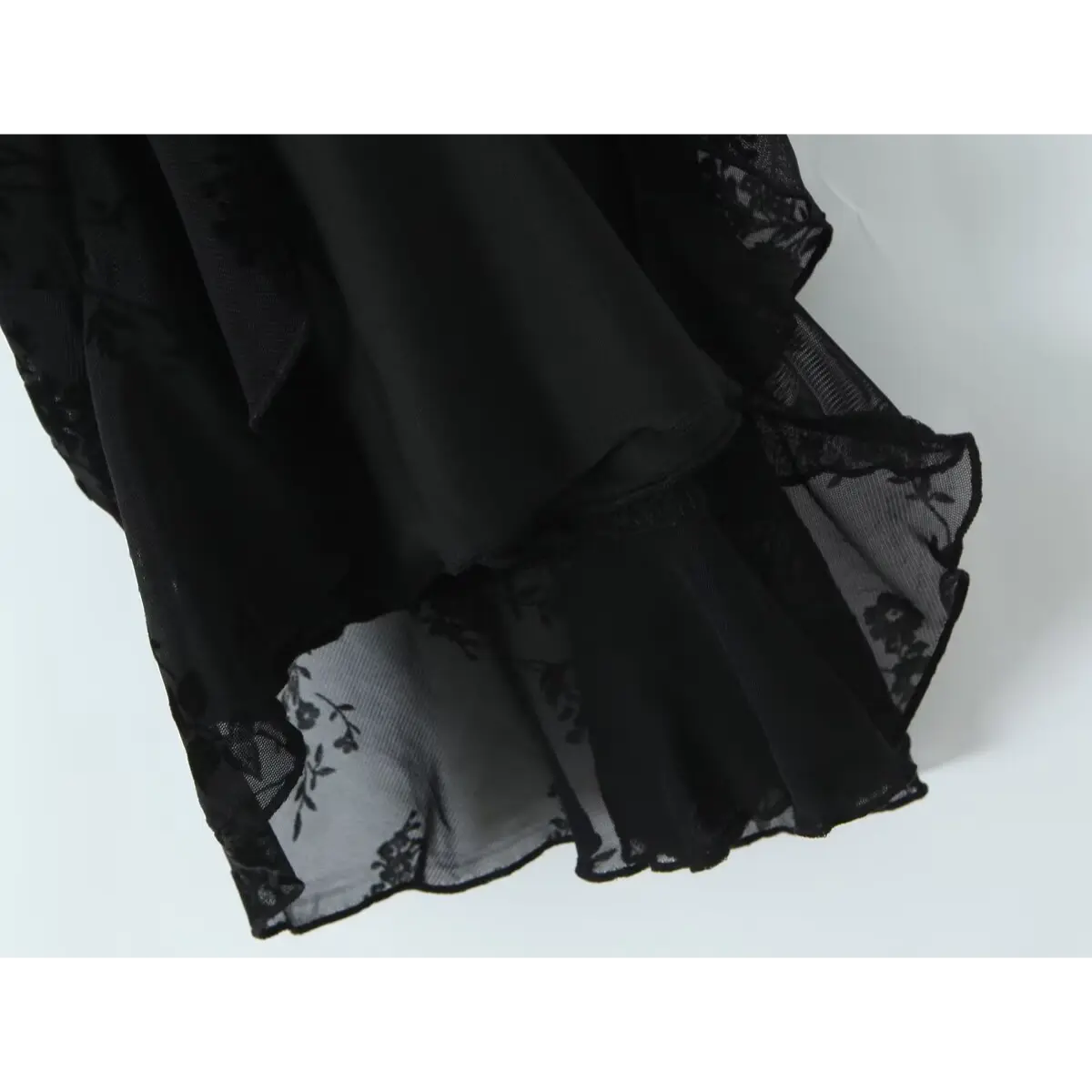 Close-up of the hem and inner lining on a black flocked floral slip dress, revealing the opaque lining and ruffled sheer overlay.