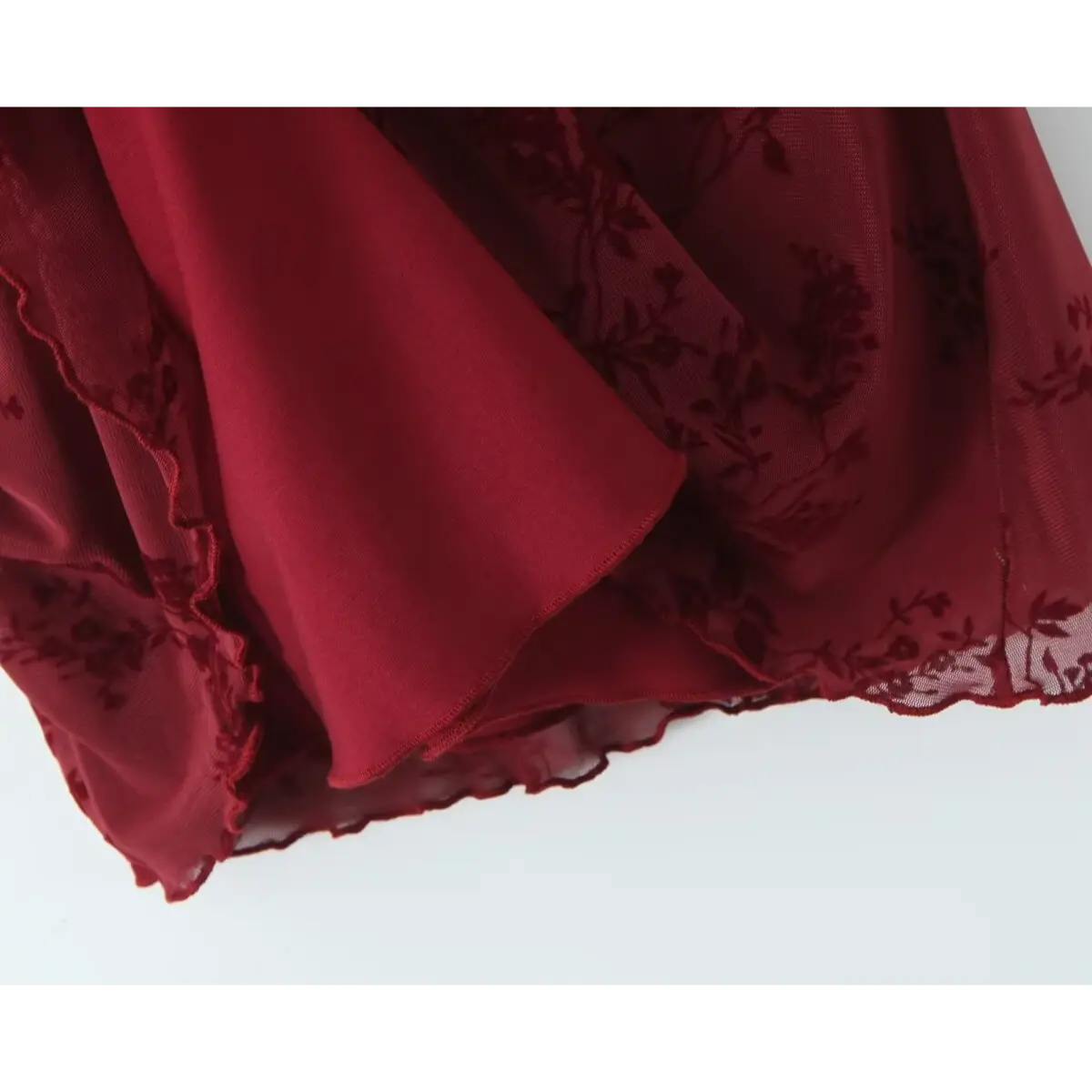 Close-up of the inner lining and ruffled hem on a burgundy flocked floral mesh dress, showing the contrast between the sheer overlay and opaque lining.