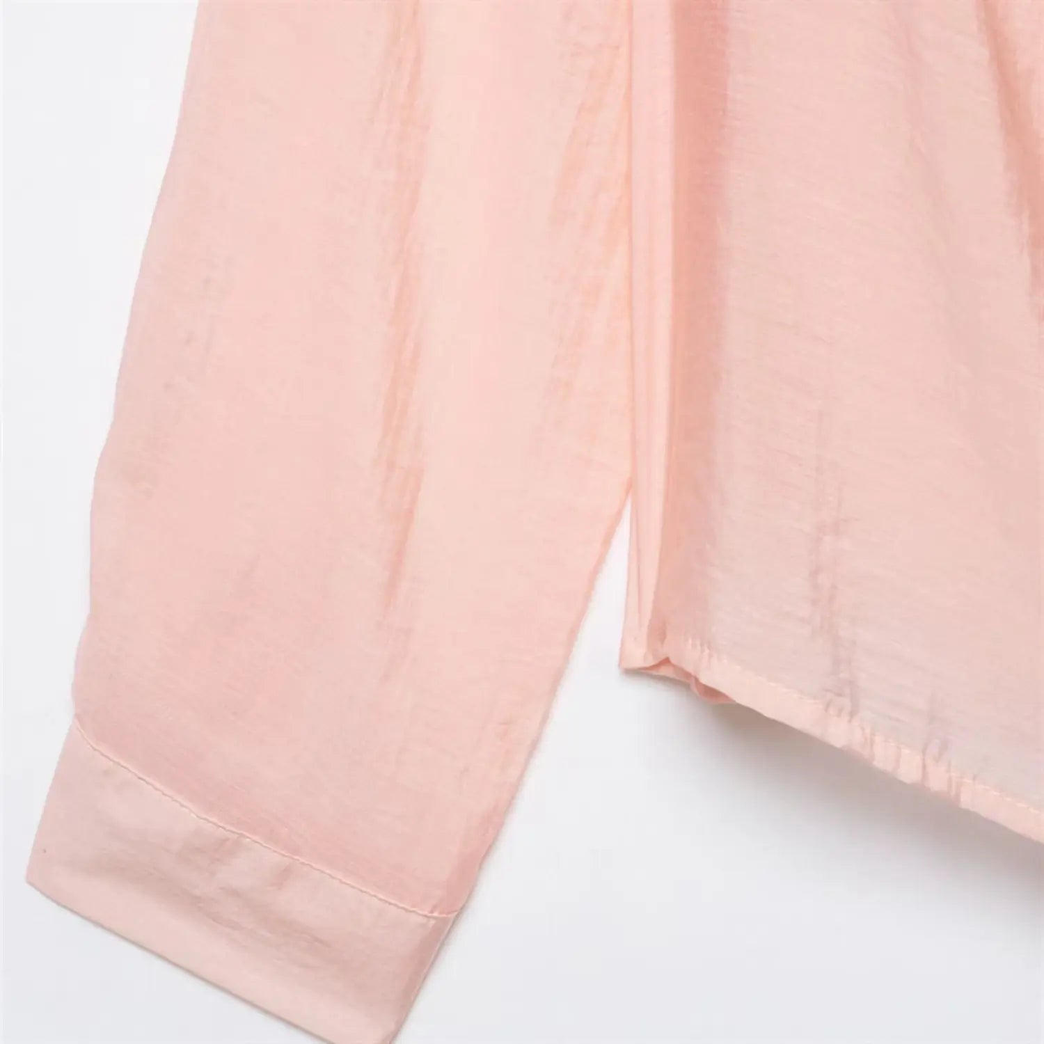Partial shot of long sleeve cuff and side torso, folded narrow cuff hem stitching, vertical side seam, lightweight shiny satin material