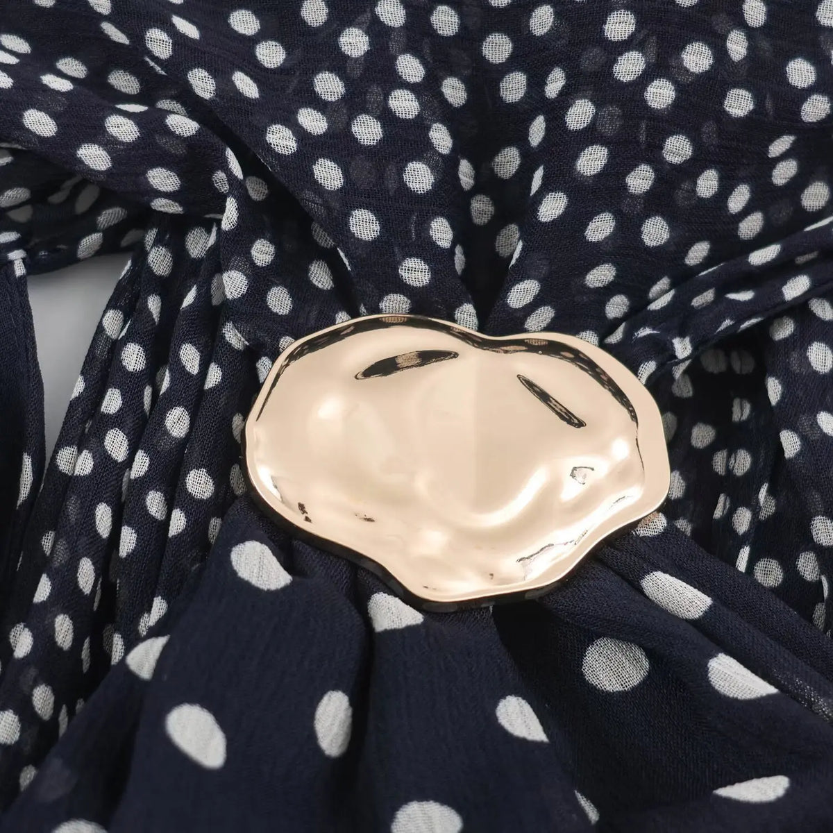 Close‑up of irregular gold metal ornament detail on halter neck polka dot maxi dress