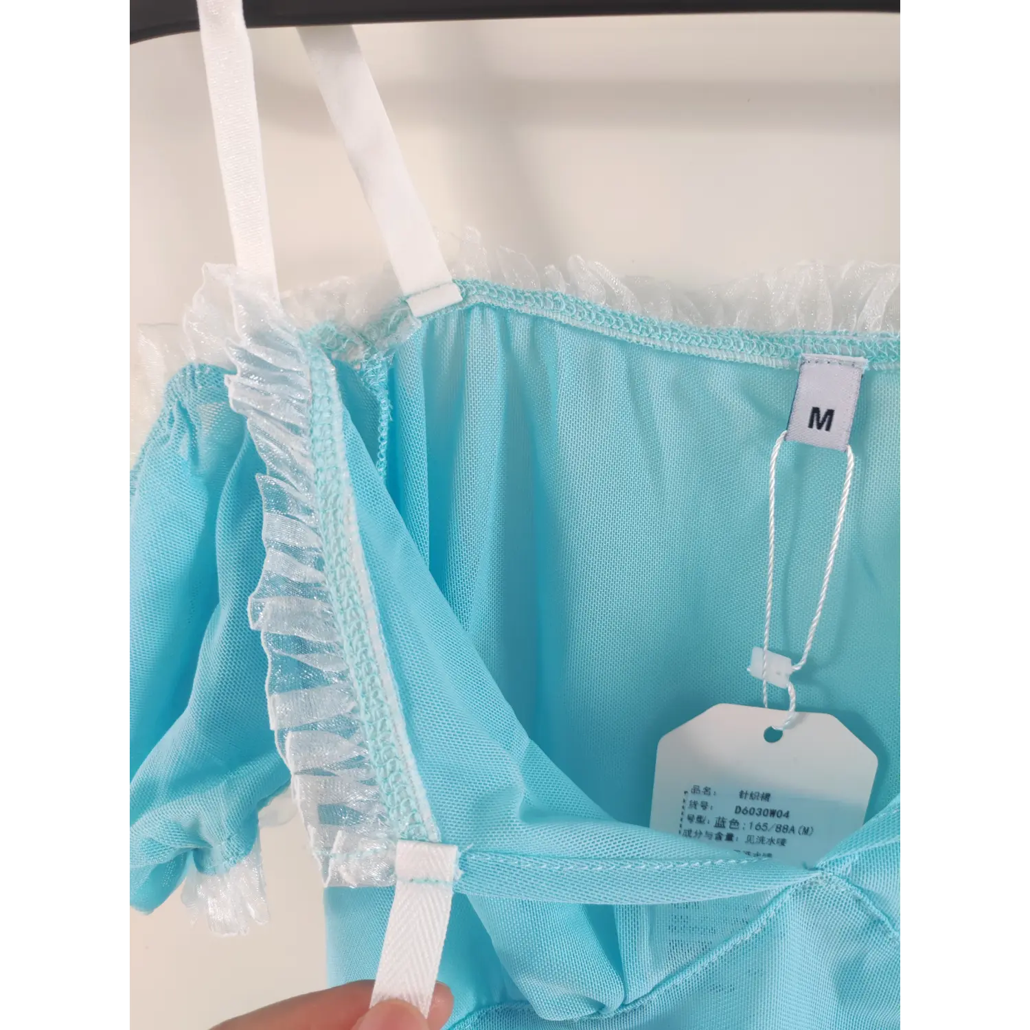 Interior shot of light blue mesh dress, M size woven label, paper hang tag, white frill v neck trim and ribbon strap