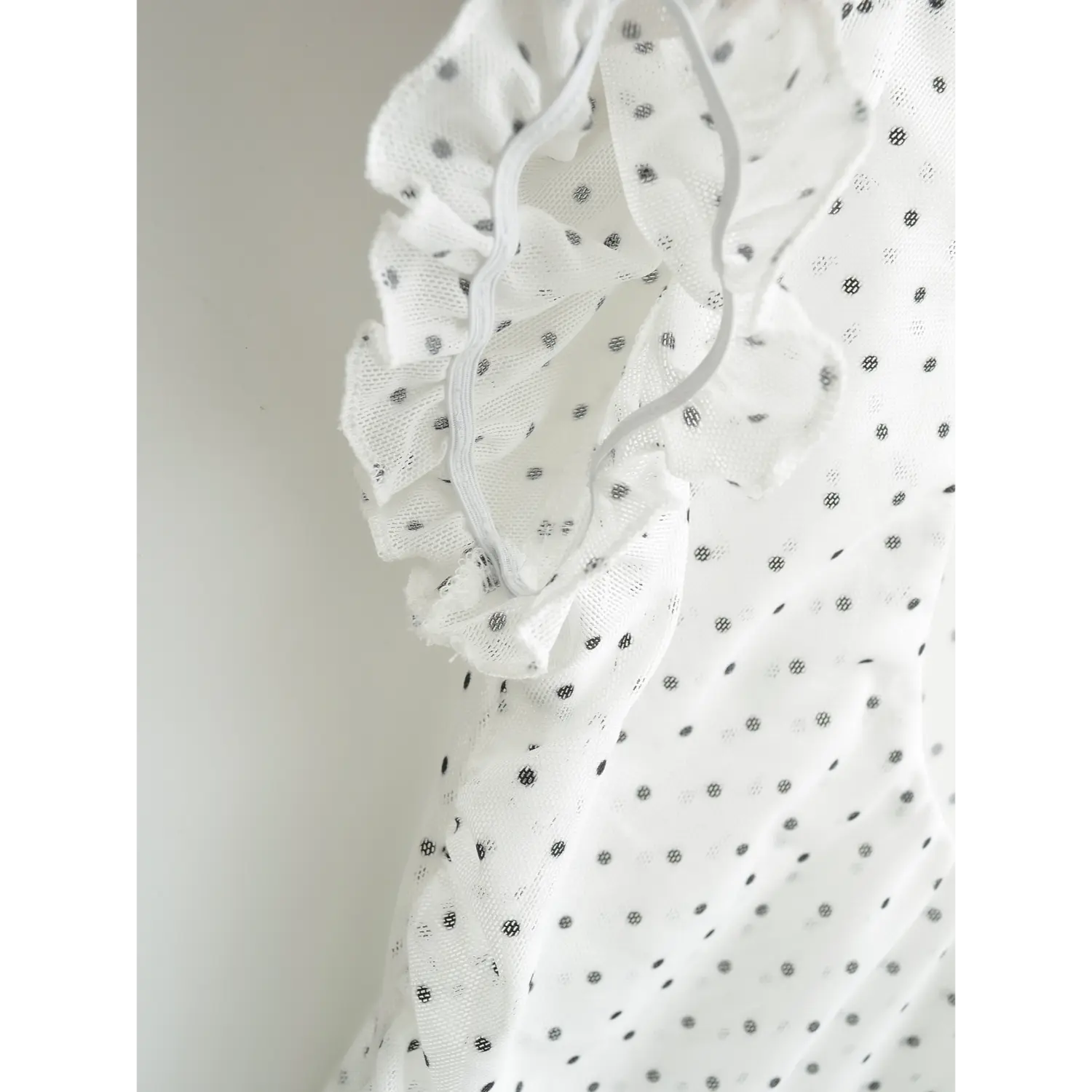 Inner lining and elastic seam close-up of frilled puff sleeve cuff, lightweight dotted mesh women’s top