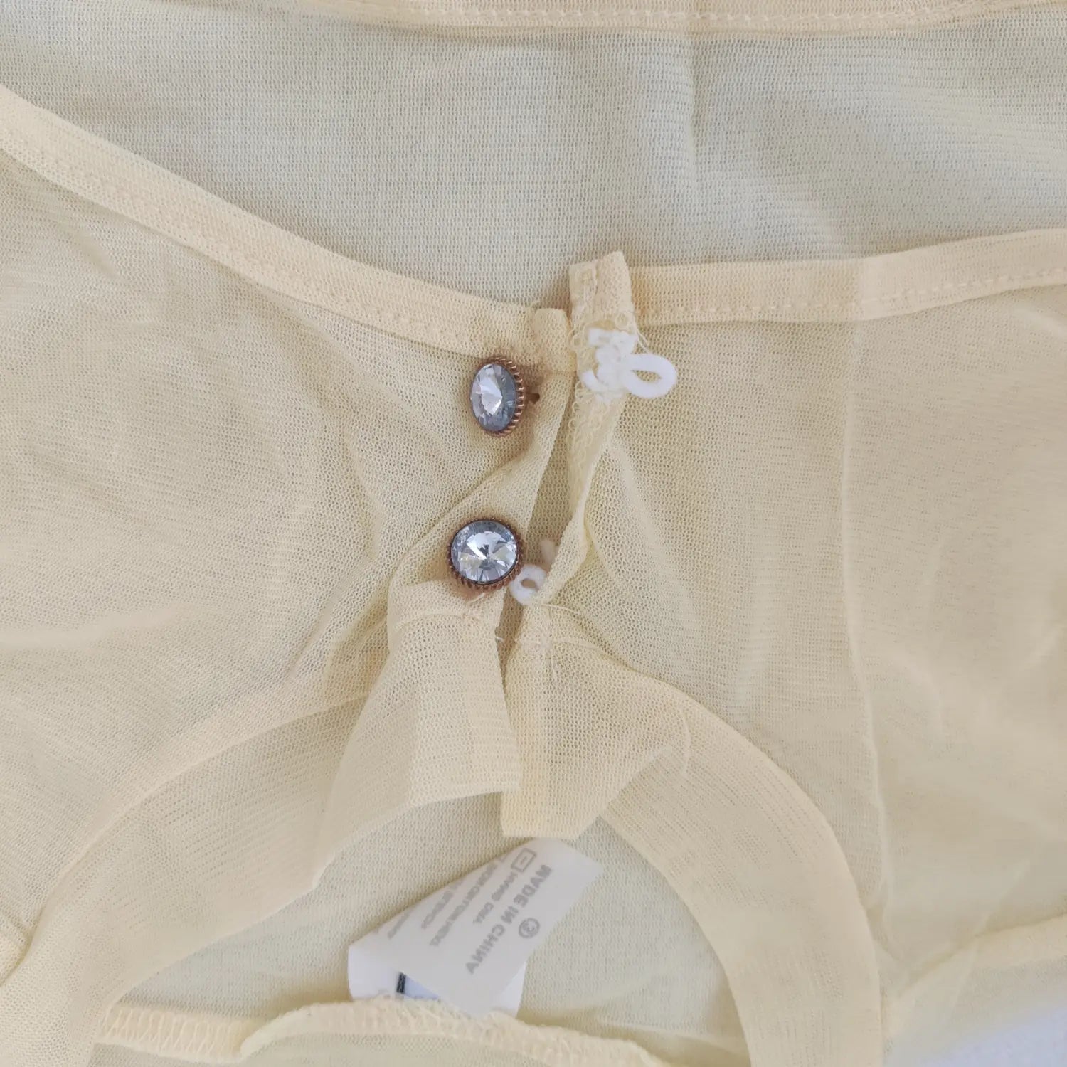 Close-up front collar, rhinestone buttons on pale yellow mesh cutout shrug