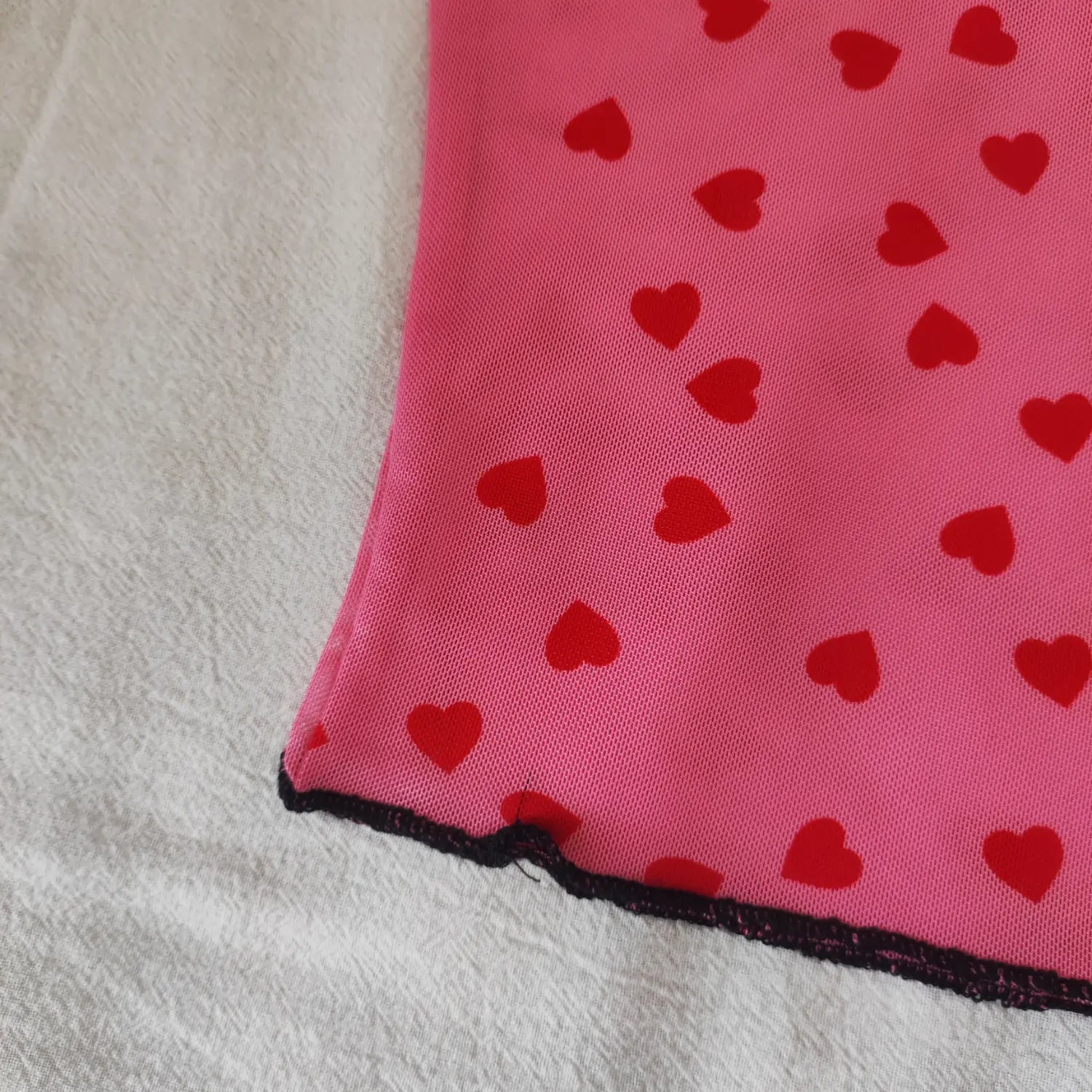 Close‑up bottom hem black lettuce trim detail of pink red heart print sheer mesh top
