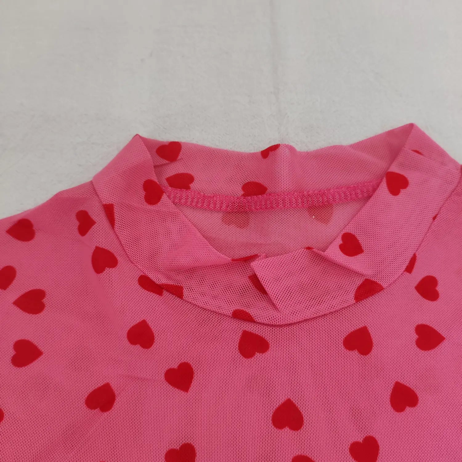 Close‑up high neck and back tab stitching detail on pink red heart print mesh top