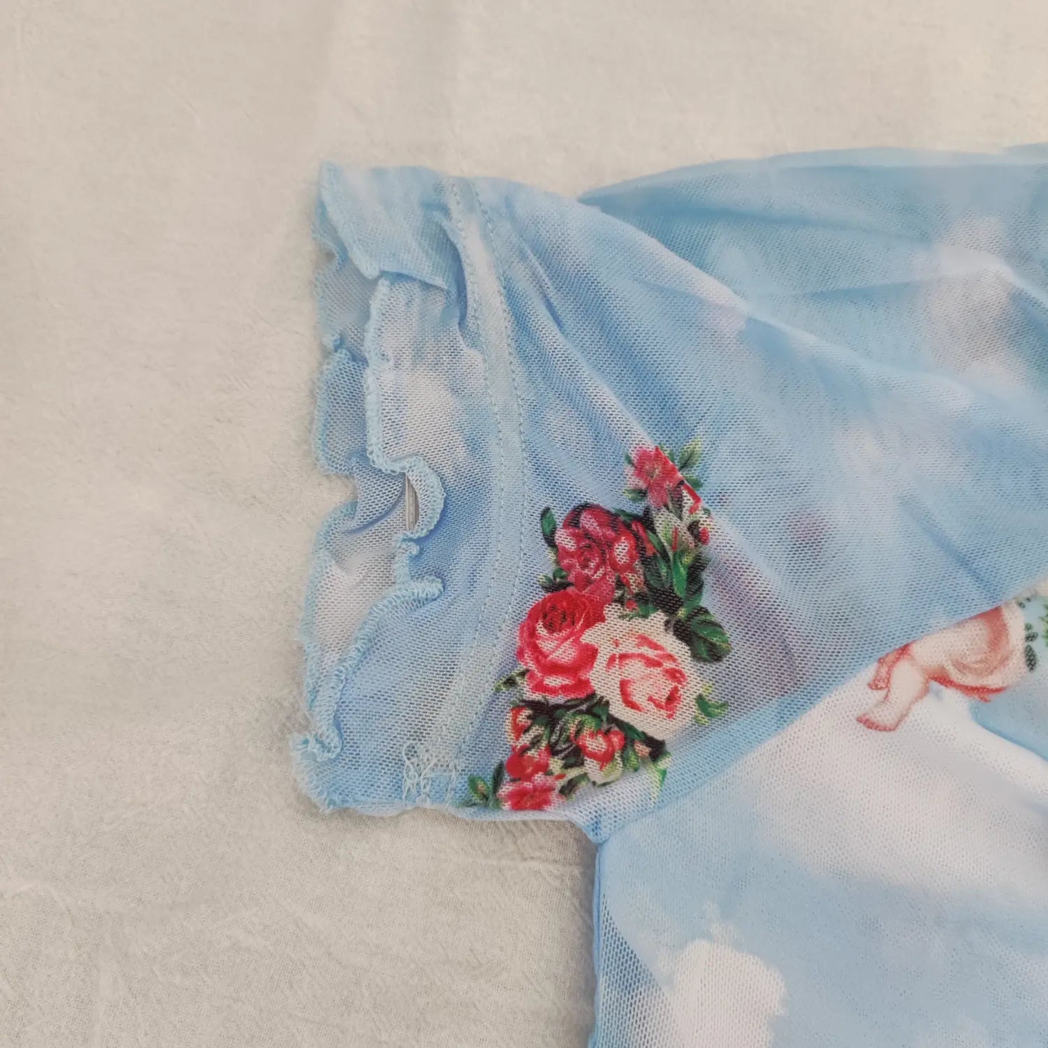 Close‑up sleeve ruffle edge and rose floral print detail of light blue cherub mesh crop top