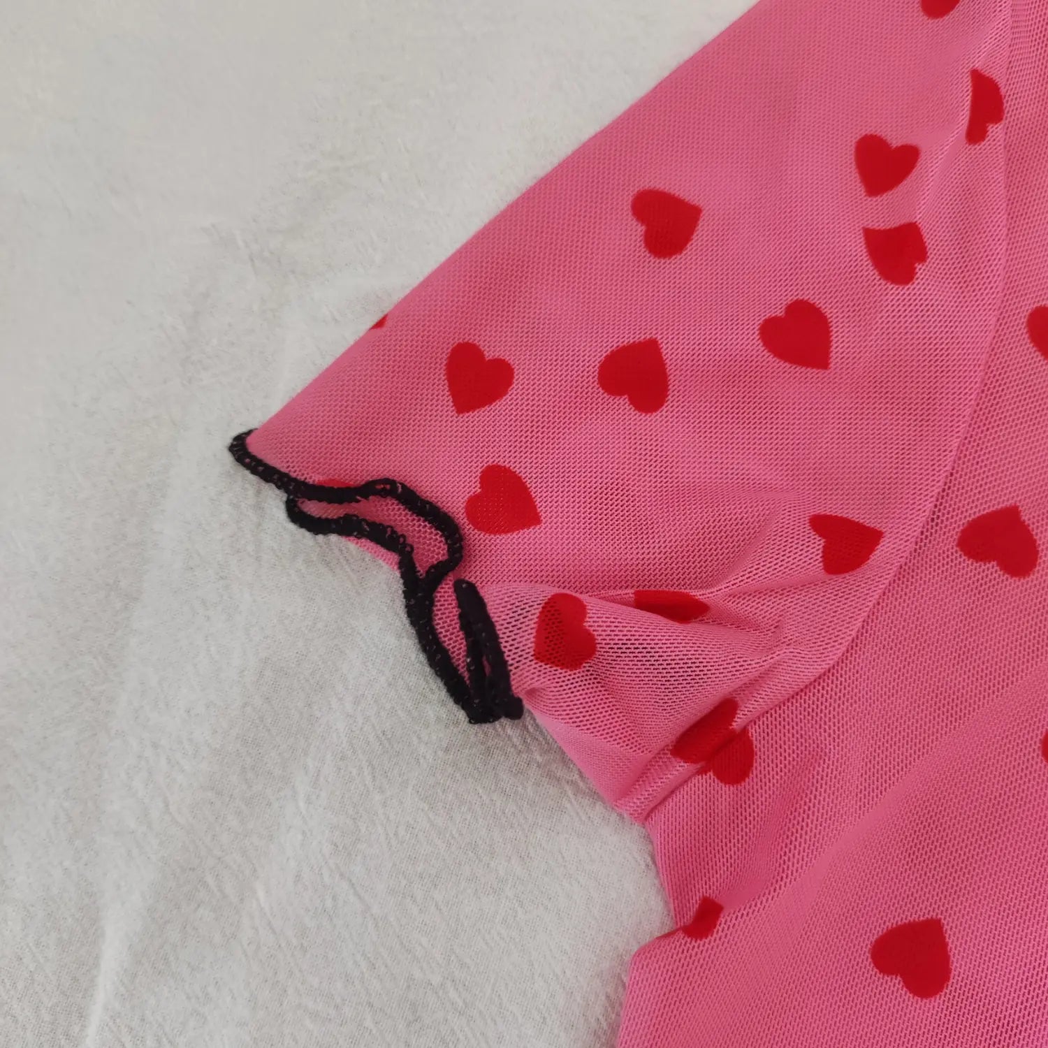 Close‑up short sleeve black lettuce ruffle cuff of pink sheer heart print mesh top
