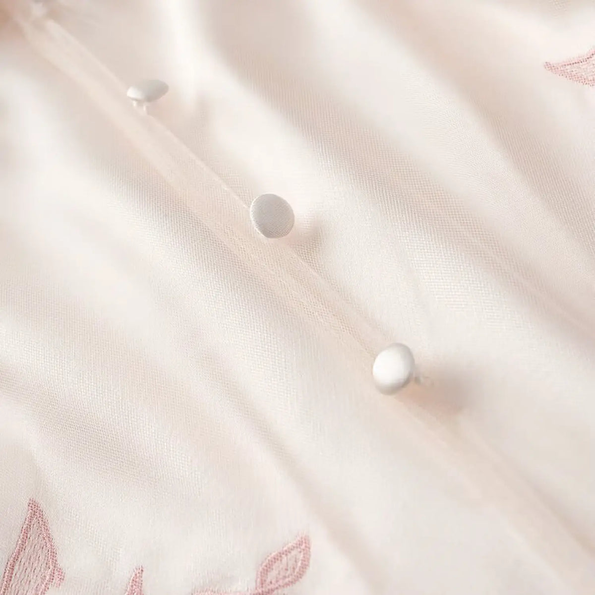 Close-up of round covered buttons on front placket of cream satin embroidered midi dress