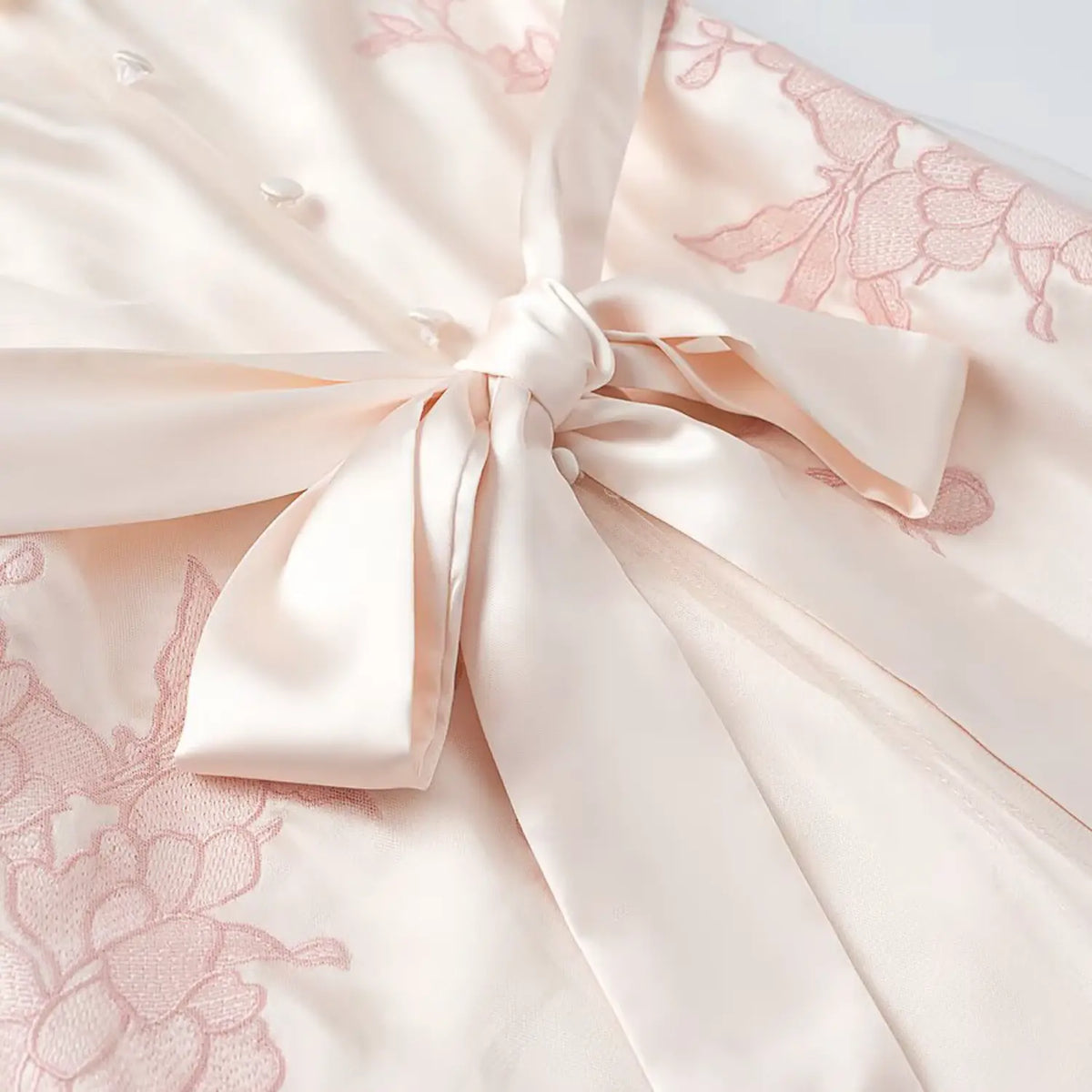 Close-up of large satin waist bow, pink floral embroidery on cream midi dress