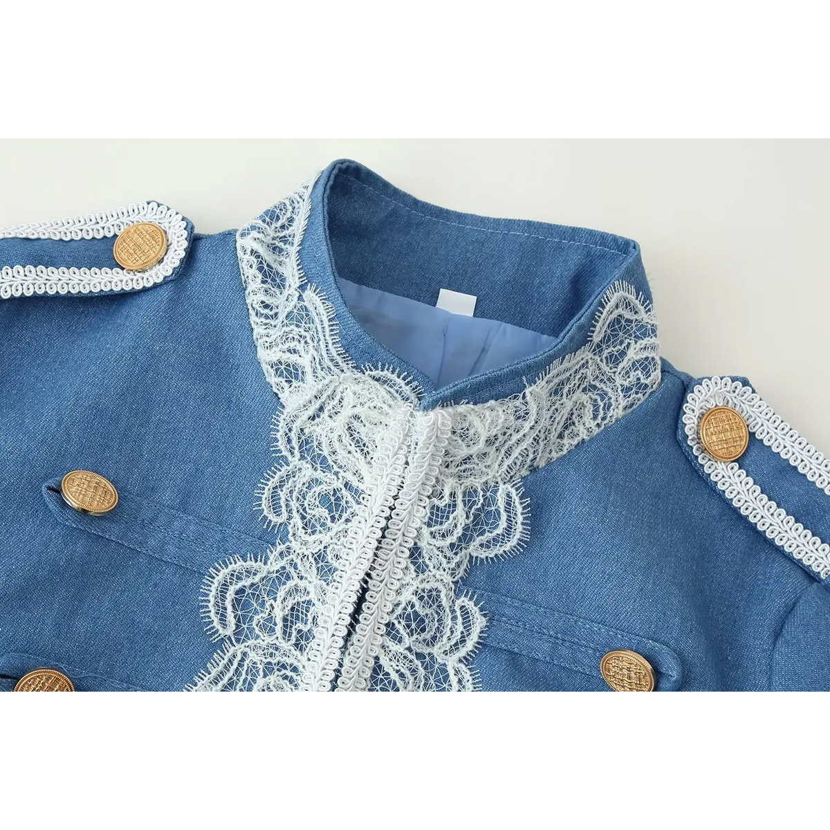 Close-up shot of stand collar and front placket, white floral lace trim and antique gold decorative buttons on blue denim fabric