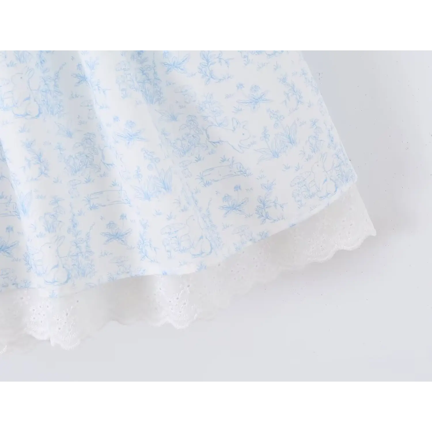 Skirt hem partial shot, outer lightweight blue rabbit floral woven fabric, inner white scalloped eyelet lace slip trim, flowy tiered hem silhouette