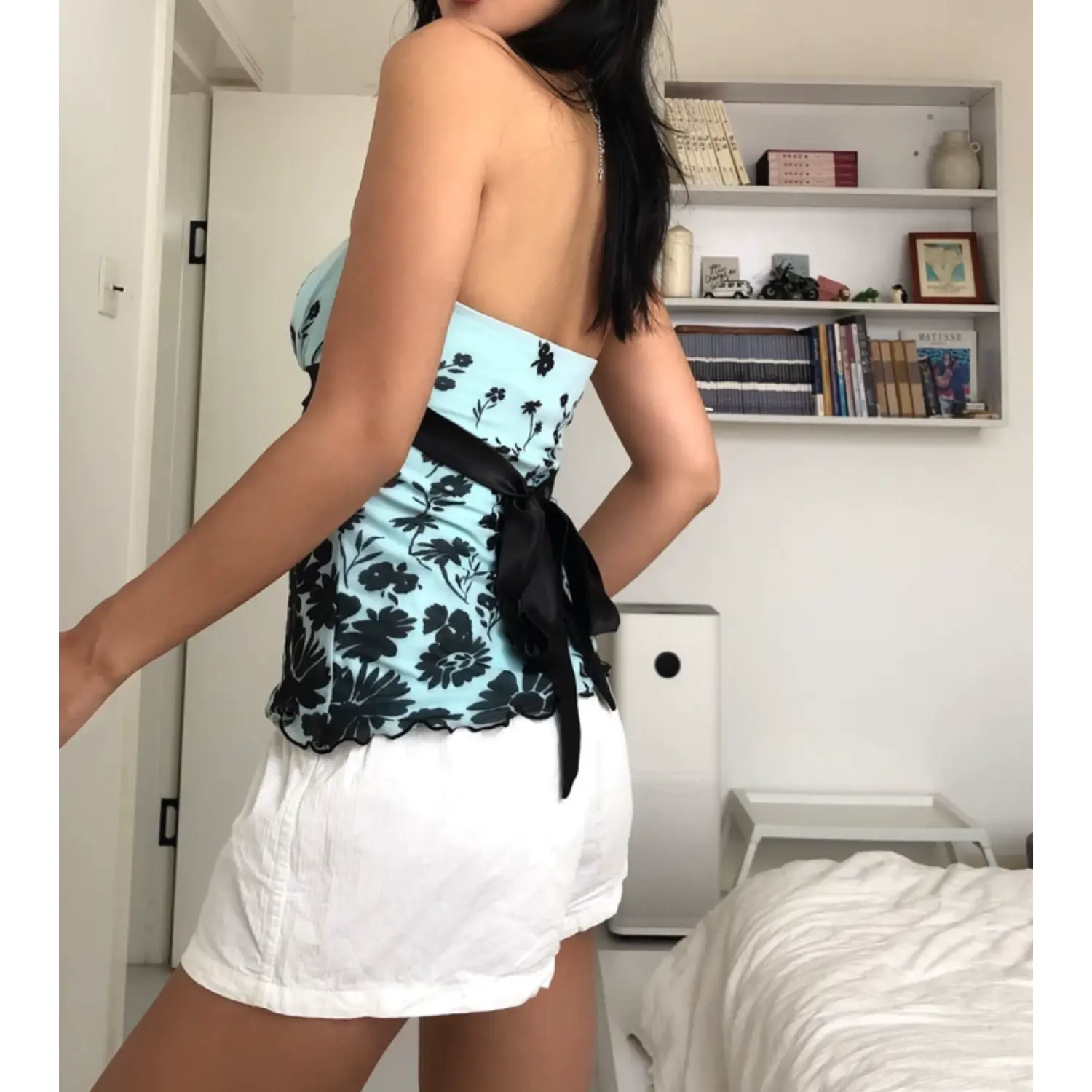 Angled static full indoor bedroom shot of stretch mesh strapless tube top, elastic gathered bust design, glossy black satin waist band, scalloped wavy mesh hem, casual daily outfit with white drawstring shorts, minimalist white room backdrop