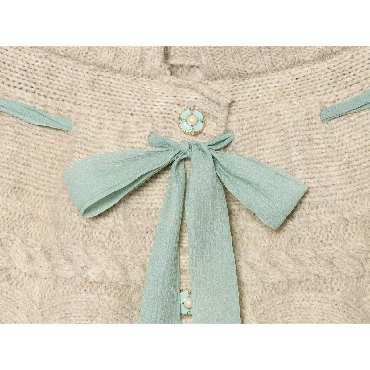 Macro detail shot of mint green chiffon bow and floral pearl buttons on oat cable knit skort