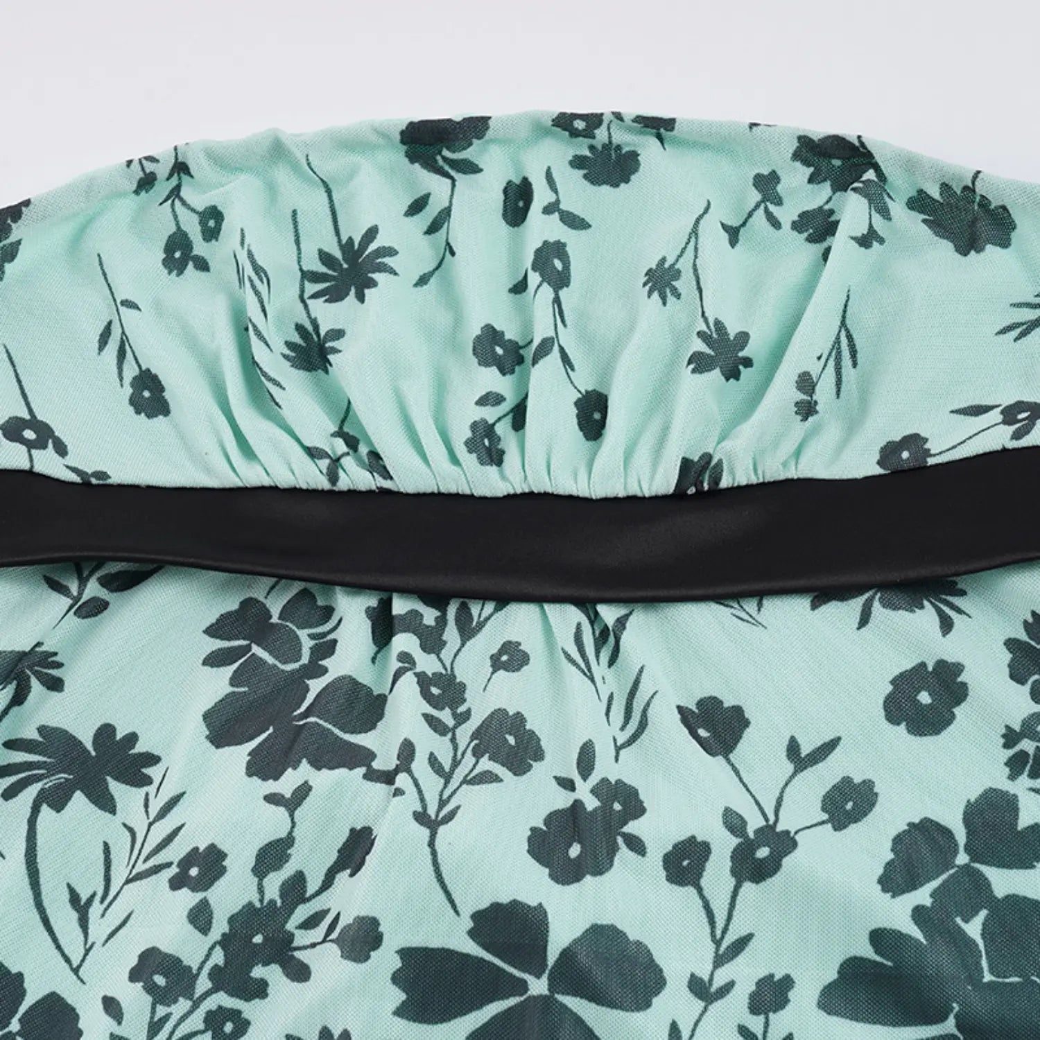 Flat lay partial shot of strapless mesh tube top, full elastic gathered upper waist, solid black wide satin waistband, allover dark green ditsy floral print on mint mesh