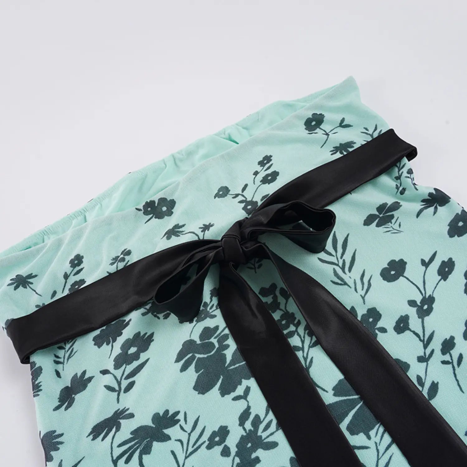 Close-up macro shot of large hand-tied black satin bow on the back of mint floral mesh strapless top, wide smooth glossy satin ribbon, soft gathered sheer mesh fabric with black flower print background