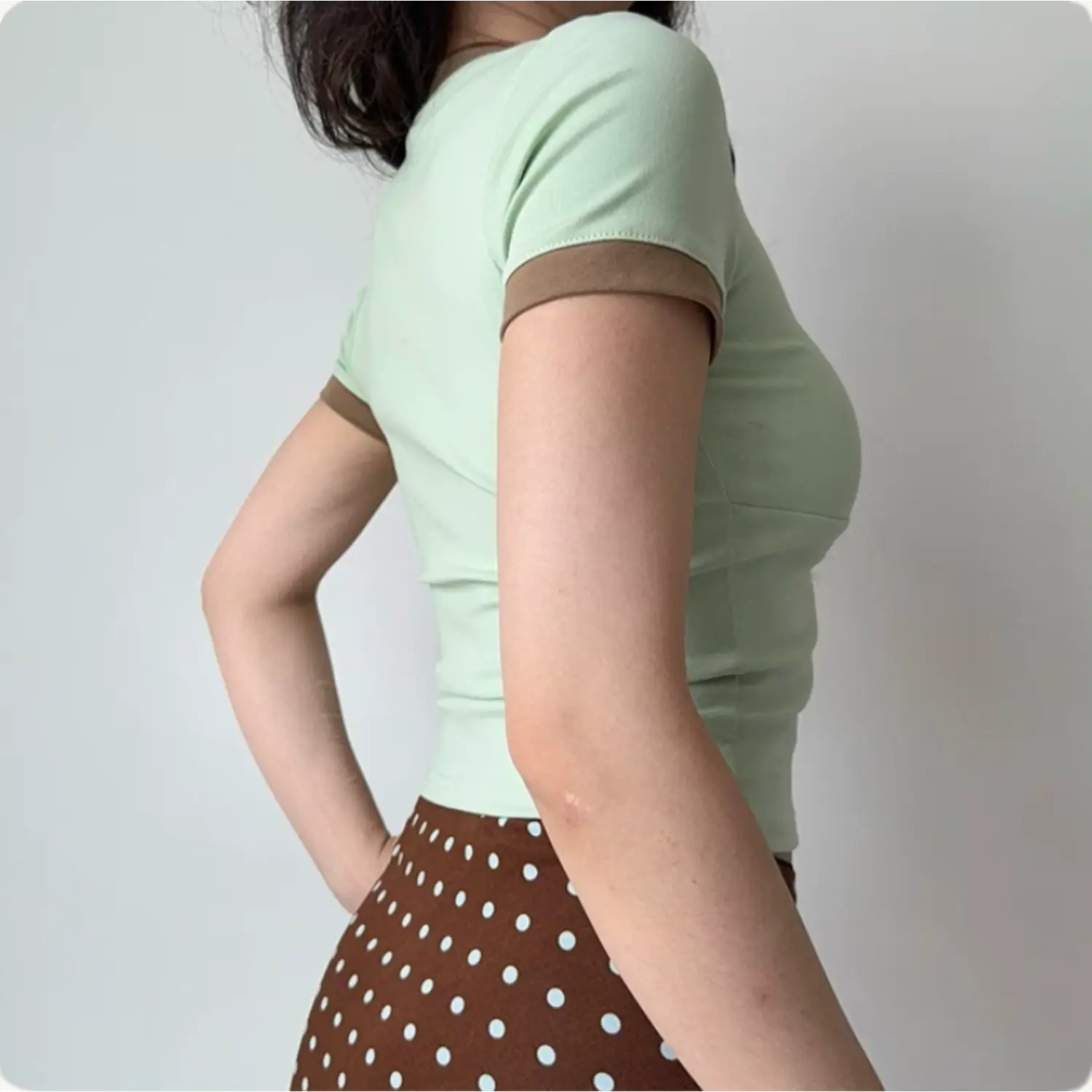 Lifestyle back shot of a woman wearing a mint green fitted V-neck tee with brown trim