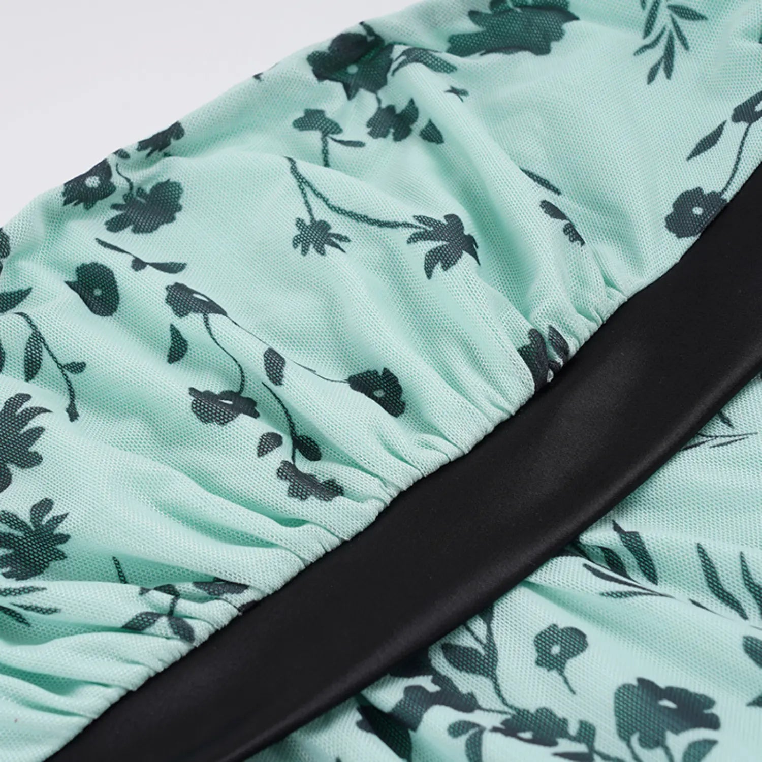 Macro close shot of mint green sheer mesh tube top fabric with dark green floral print, elastic gathered waist band, wide smooth black satin ribbon trim, lightweight breathable mesh texture