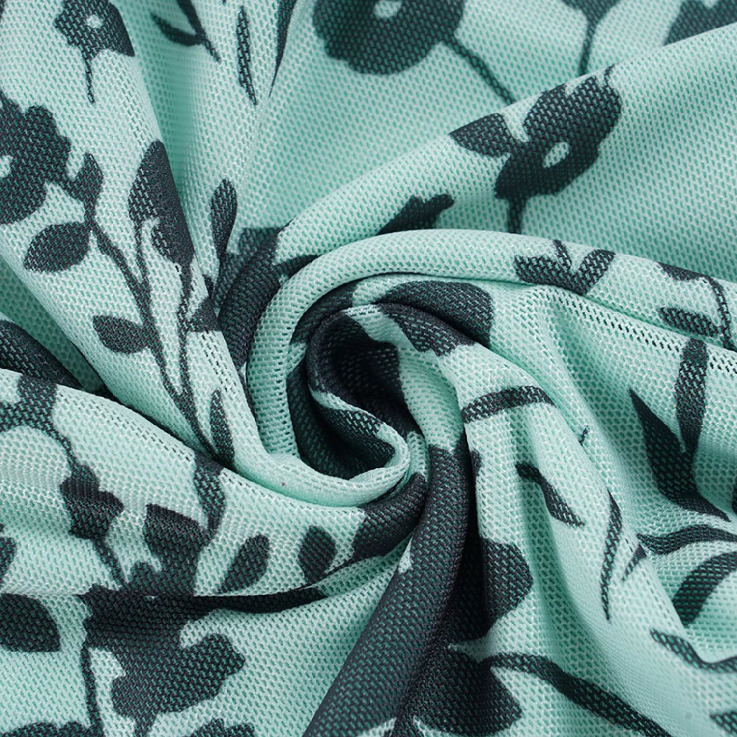 Twisted folded texture close-up of mint sheer mesh fabric, all-over dark green scattered floral print, soft stretch mesh weave showing drape and breathability