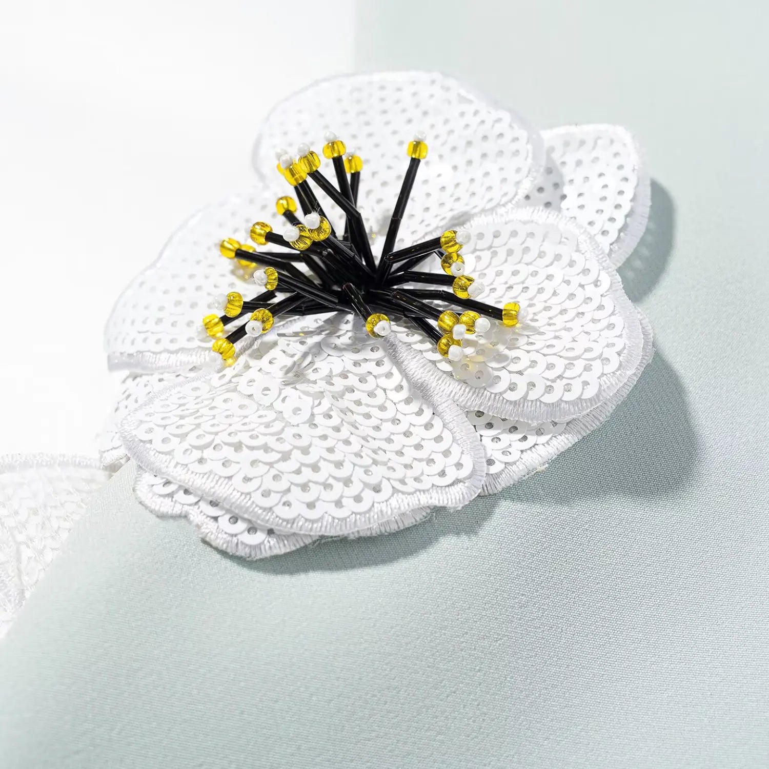 Close-up shot of the white sequined flower appliqué on a mint green sleeveless dress, showing the beaded center detail