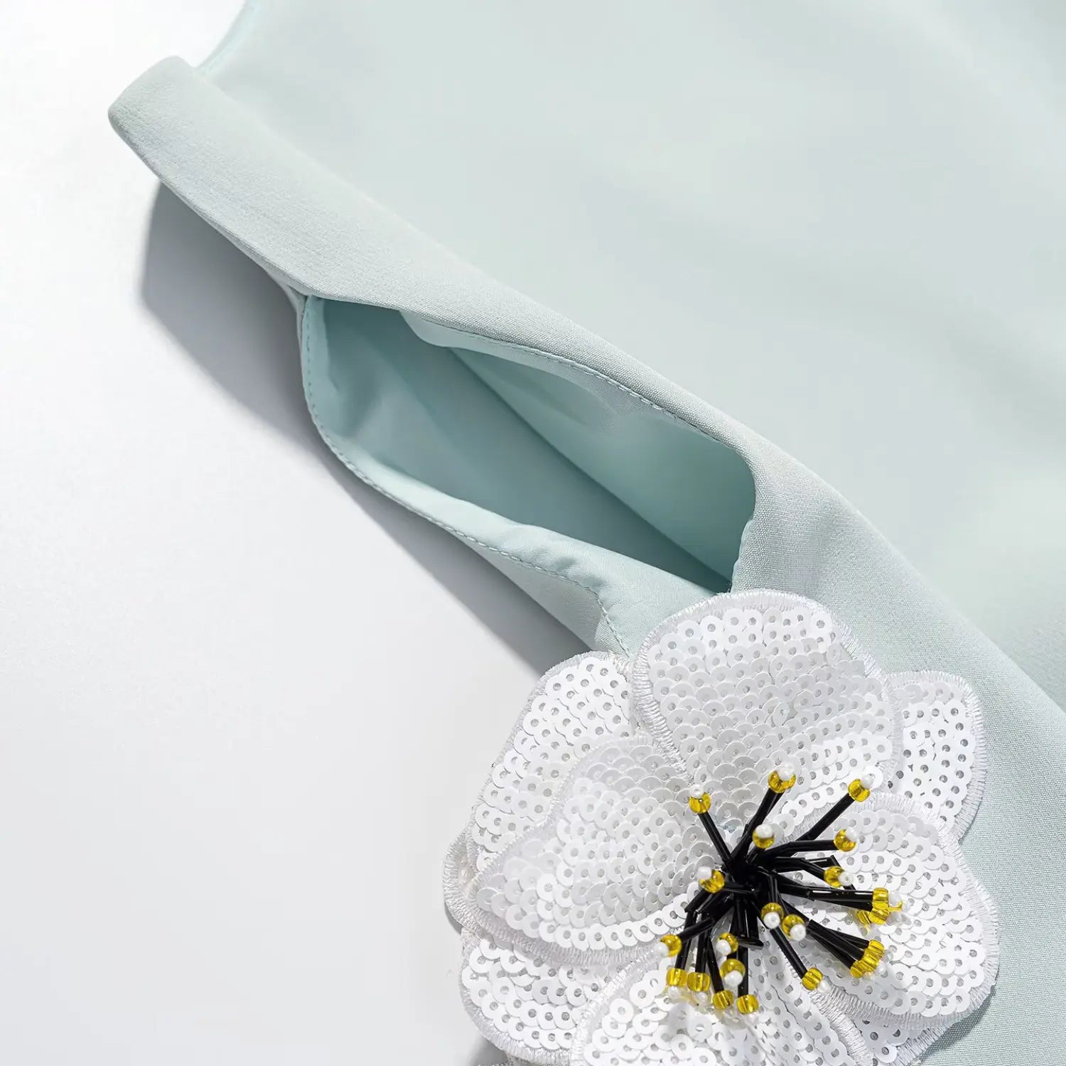Close-up shot of the mint green sleeveless dress's armhole and the attached sequined flower appliqué