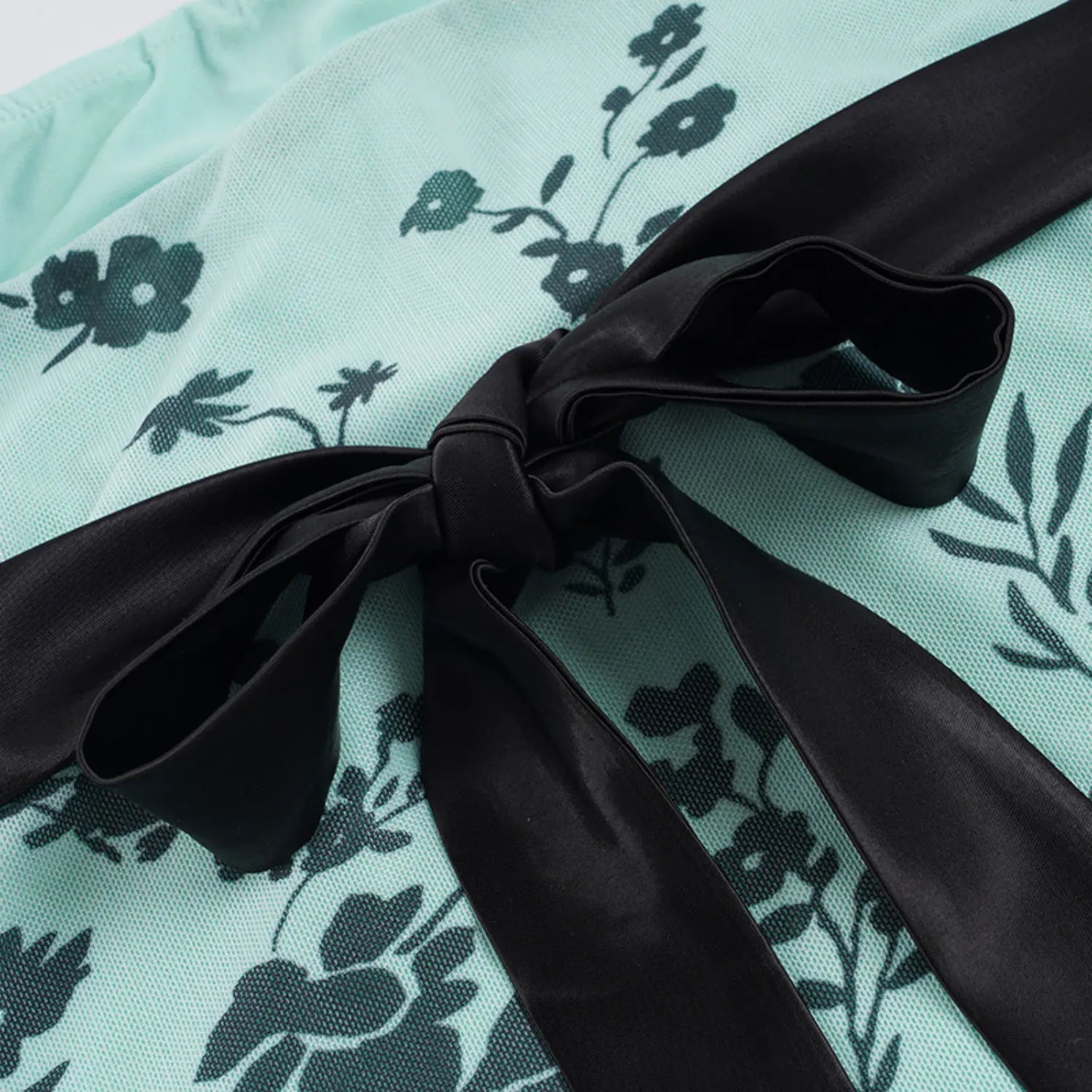 Close-up of large hand-tied black satin bow on the back of mint floral mesh strapless top, wide smooth satin ribbon, soft gathered mesh fabric background