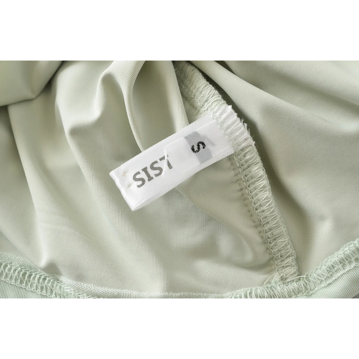 Close up of clothing label tag on mint green halter ruched bodycon mini dress, inner lining and stitching detail