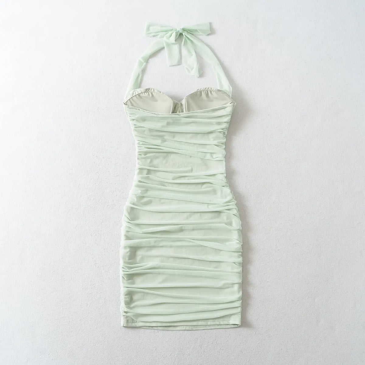 Back view flat lay of mint green halter ruched bodycon mini dress, halter self tie bow and padded cups