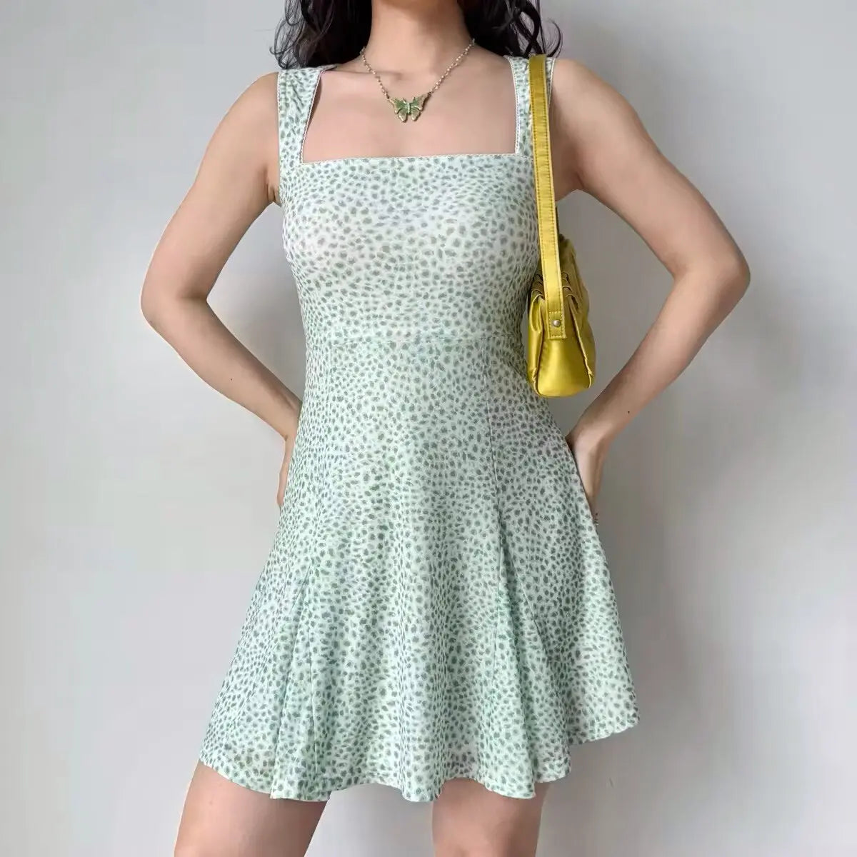 Woman in a mint green leopard print flare mini dress, carrying a yellow shoulder bag, showing the dress's form-fitting silhouette and pattern.