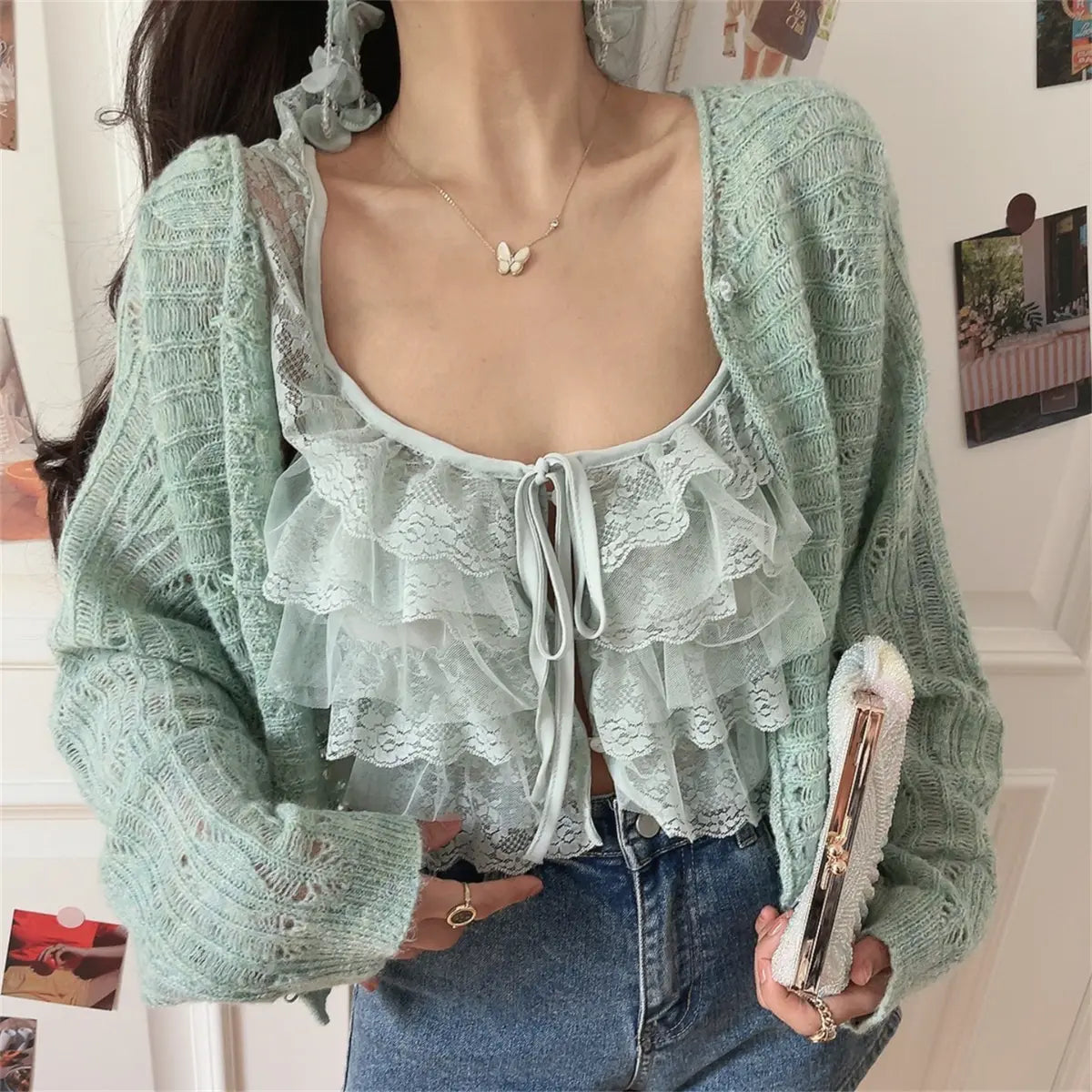 Close-up view of a mint green openwork knit cardigan worn over a matching lace ruffled camisole, paired with jeans, holding a pastel rainbow beaded clutch.