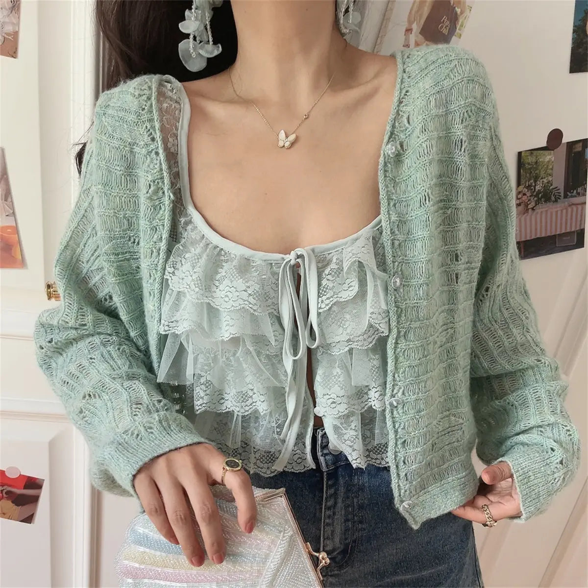 Front view of a mint green openwork knit cardigan worn over a matching lace ruffled camisole, paired with jeans, with a pastel rainbow beaded clutch.