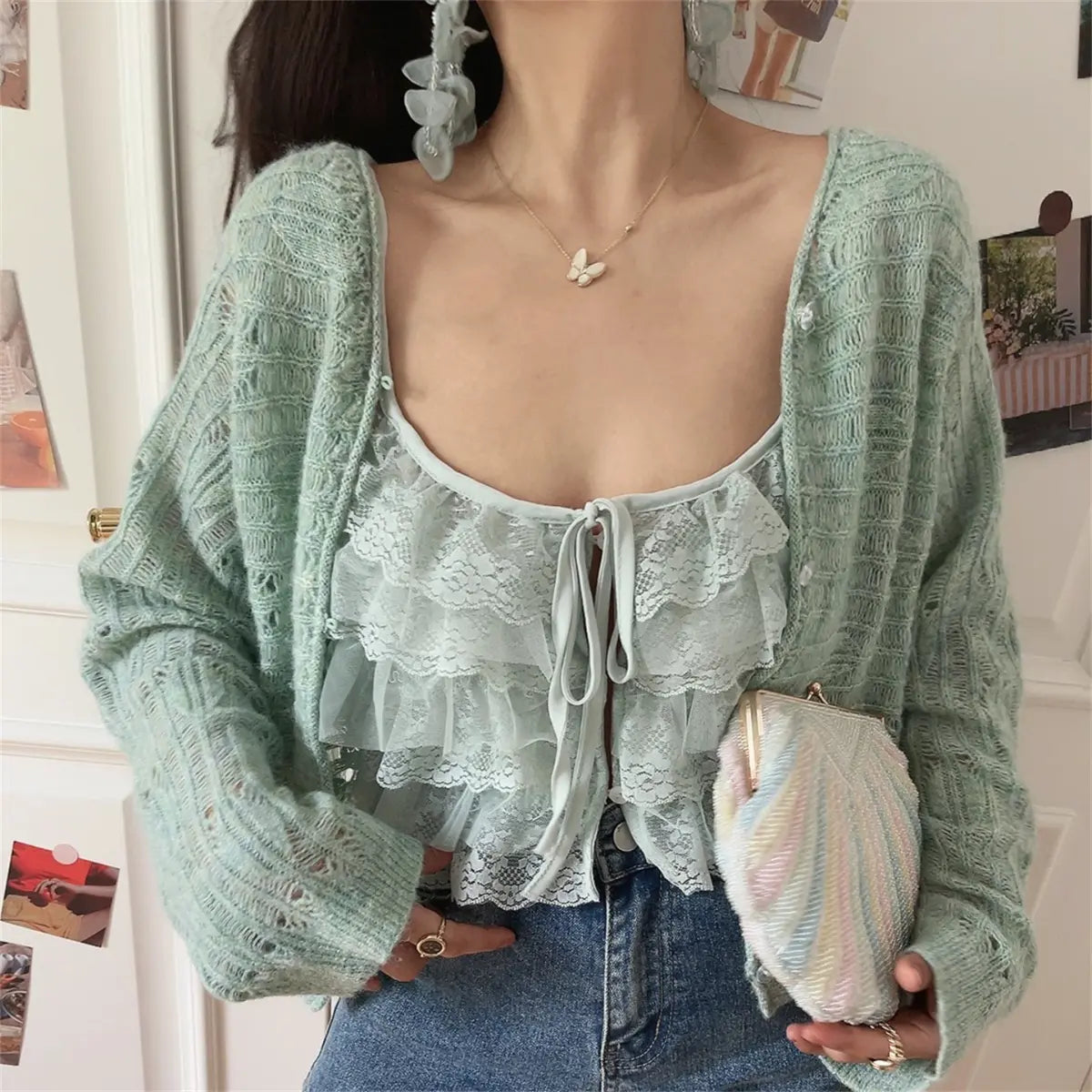 Model wearing a mint green openwork knit cardigan over a matching lace ruffled camisole, paired with jeans, holding a pastel rainbow beaded clutch.