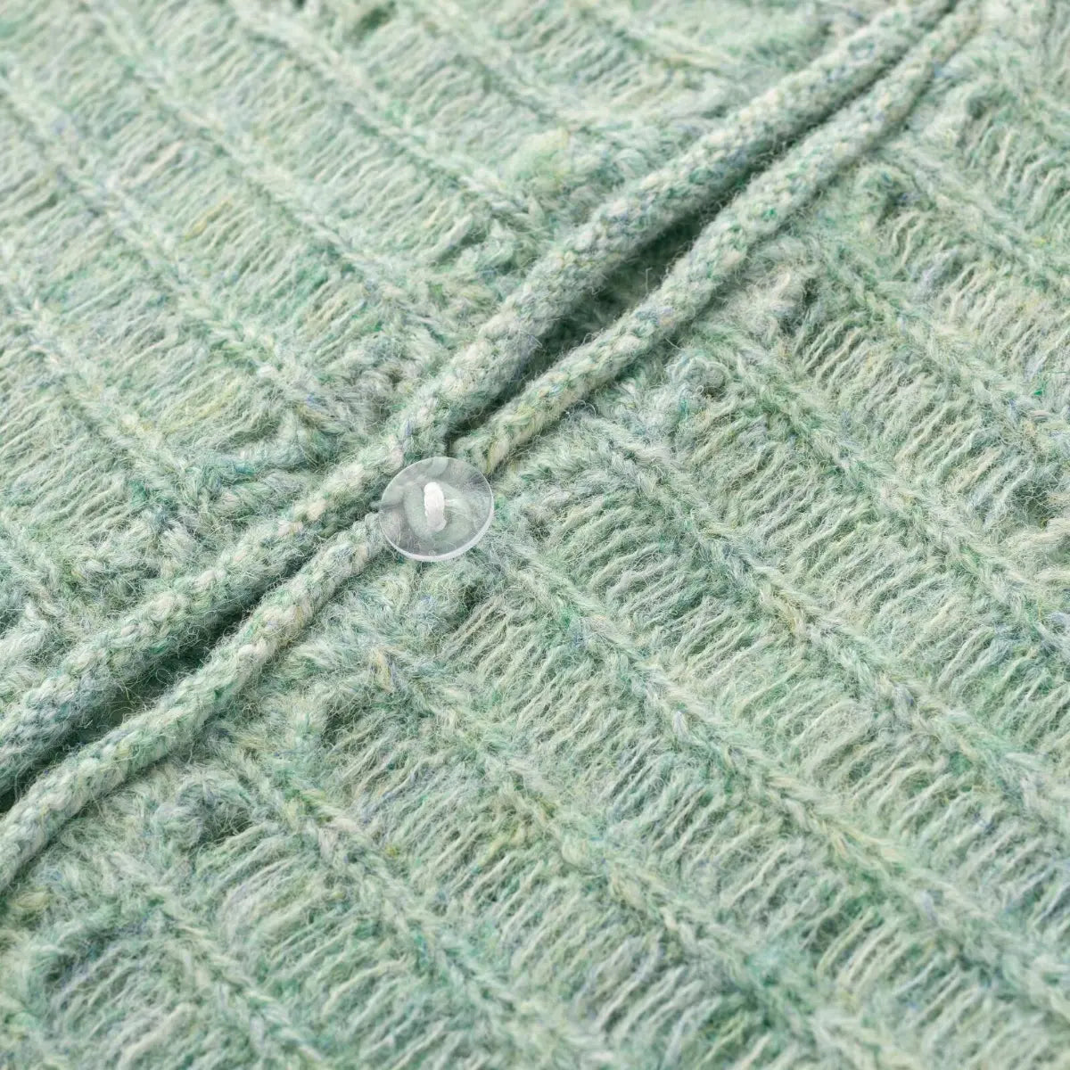 Close-up of a transparent button on a mint green openwork knit cardigan, showing how it fastens the front placket.