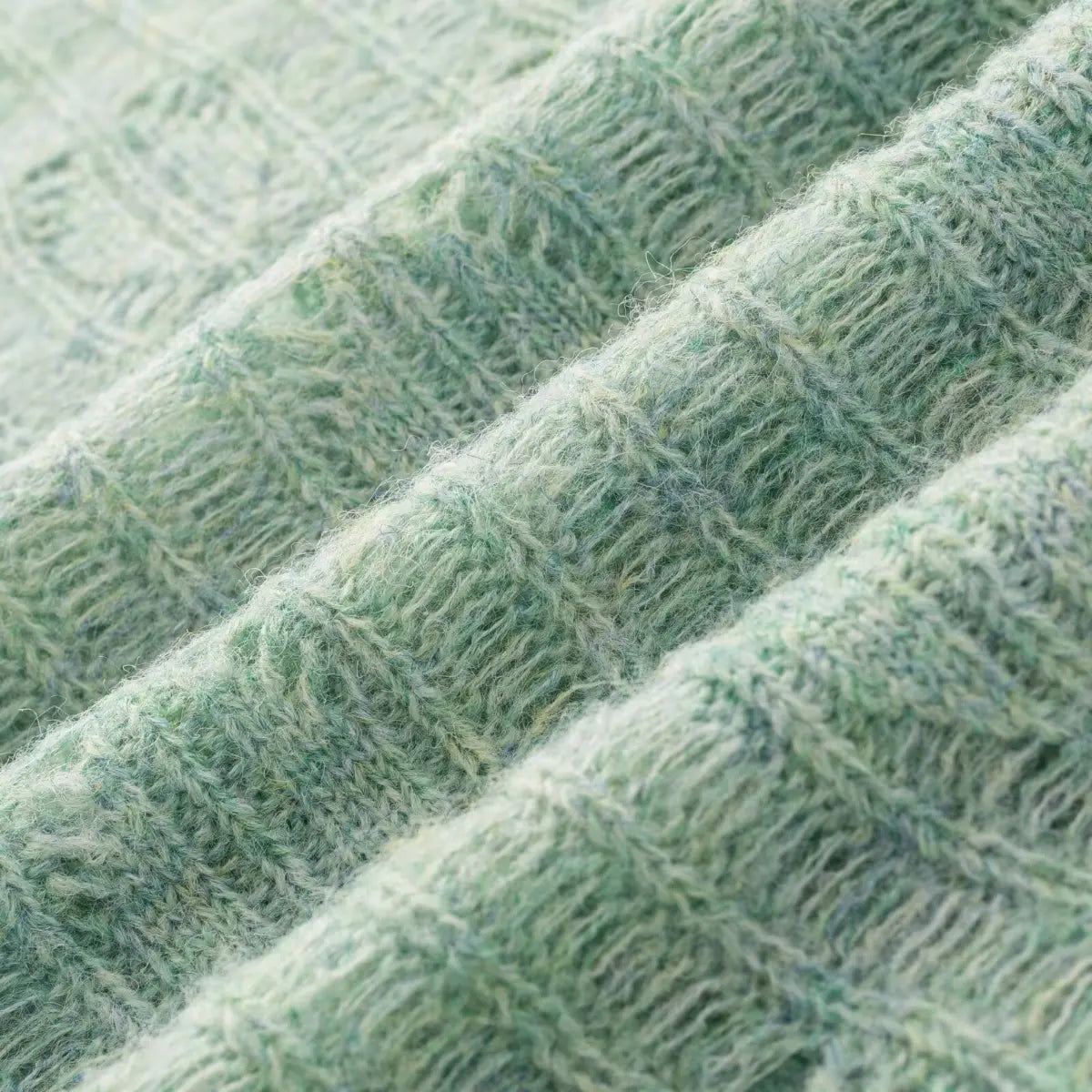 Close-up view of the soft, marled fabric texture of a mint green openwork knit cardigan, highlighting its fuzzy, multi-tonal appearance.