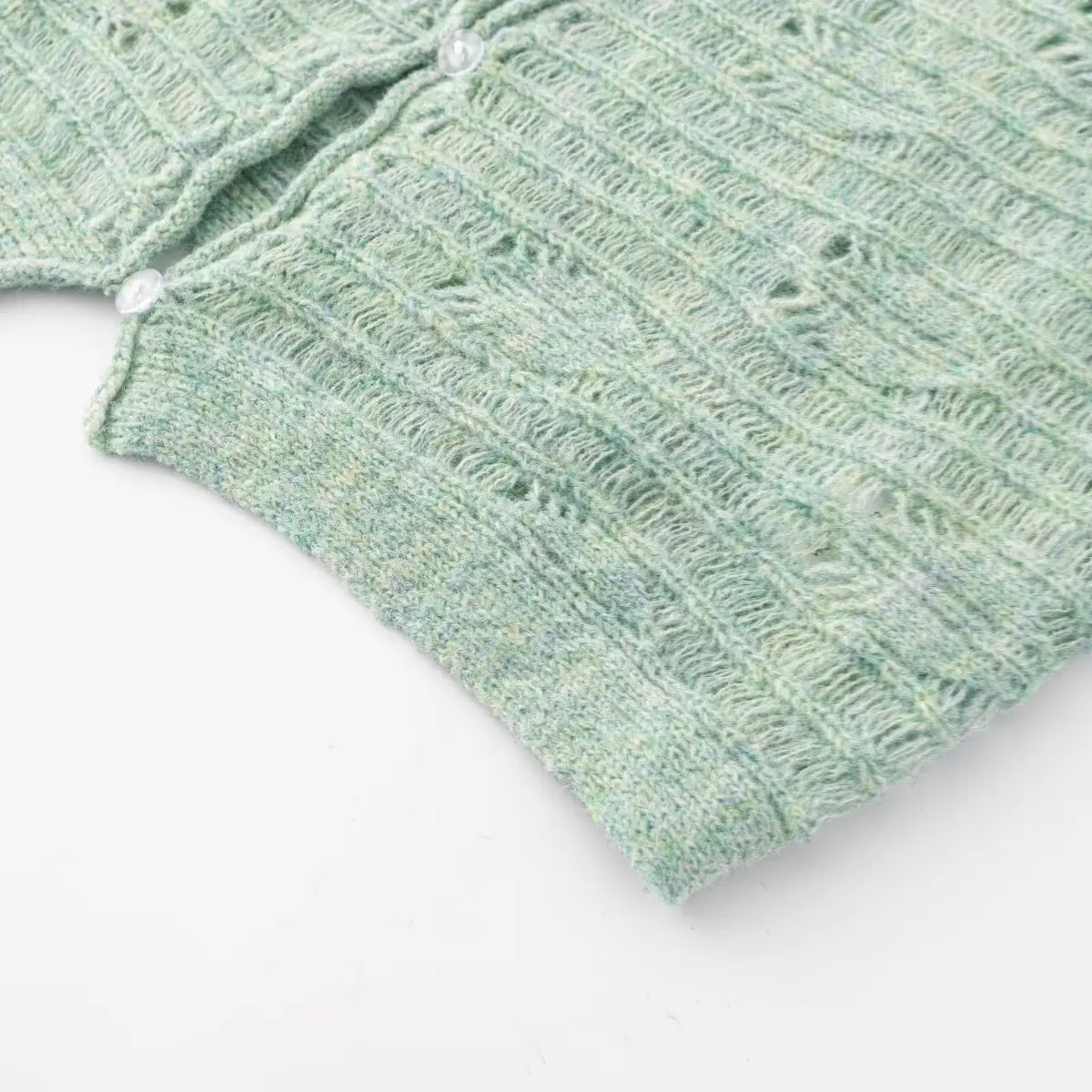 Close-up detail of the bottom hem of a mint green openwork knit cardigan, showing the finished knit edge.