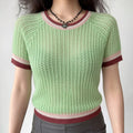Front lifestyle shot on model, light mint green openwork mesh knit short sleeve top, round neck with pink-white-burgundy striped trim, raglan sleeves, cropped fitted hem, matched with grey bottoms and heart pendant necklace, casual summer daily outfit